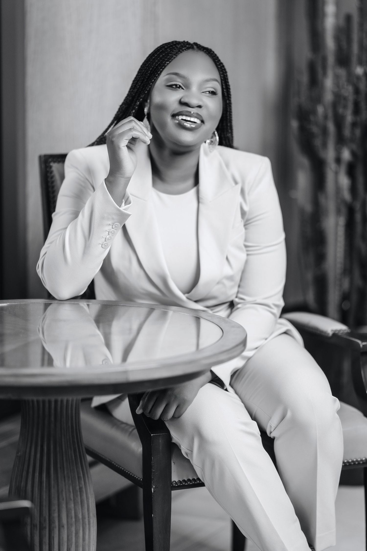 Professional black and white portrait of a person in a white blazer sitting at a round table with a warm smile.
