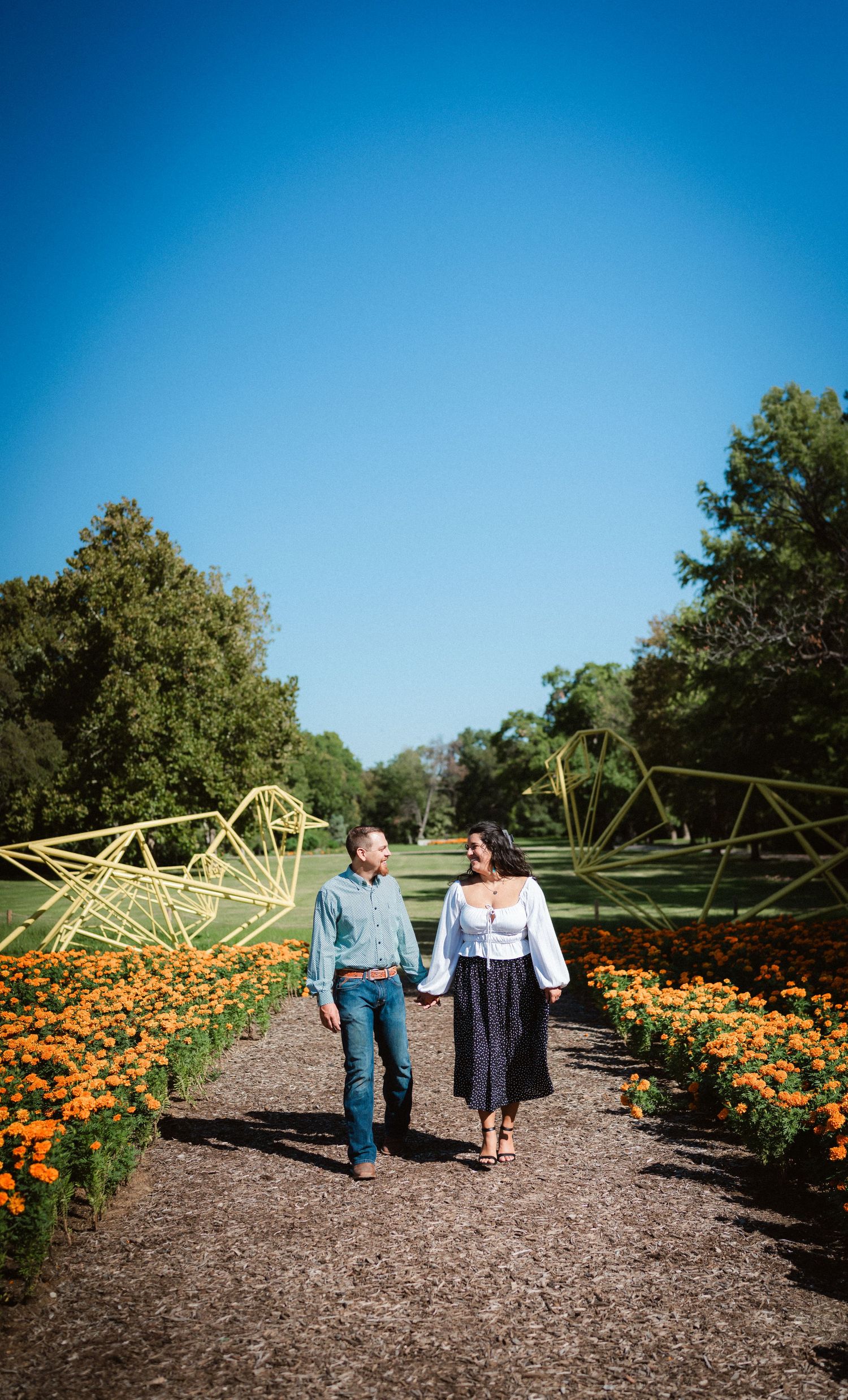 A couple walks through a garden path lined with vibrant orange marigolds and green archways.
