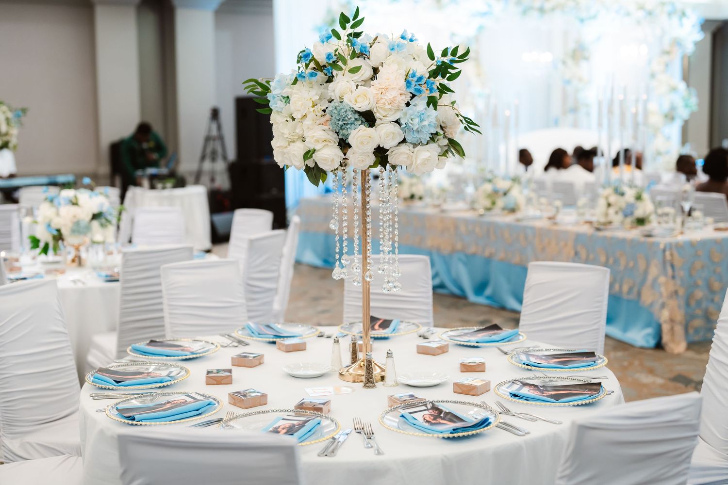 Wedding reception table decorated in white and blue with tall floral centerpieces and elegant place settings.