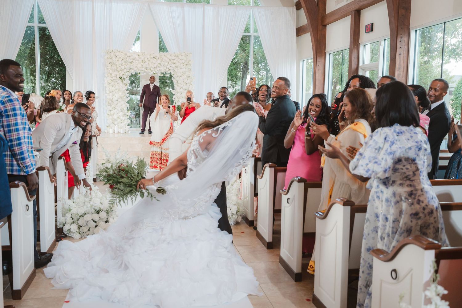 Wedding ceremony procession in a light-filled venue with white draping and floral decorations.