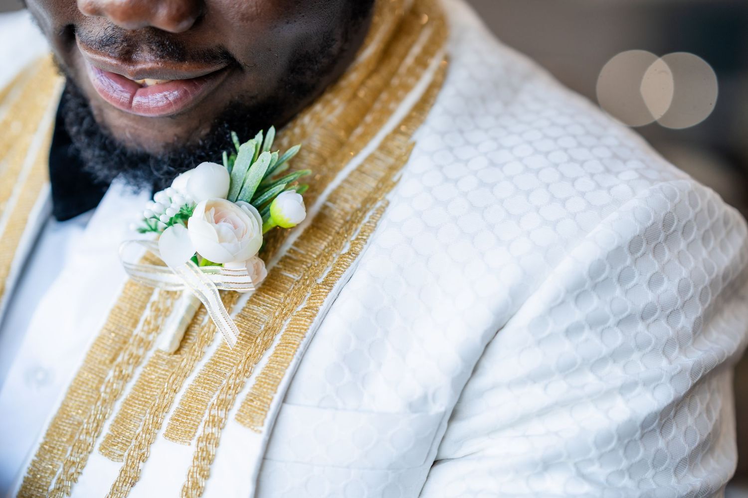 A smiling person wearing a white suit and gold patterned vest poses for a formal portrait.