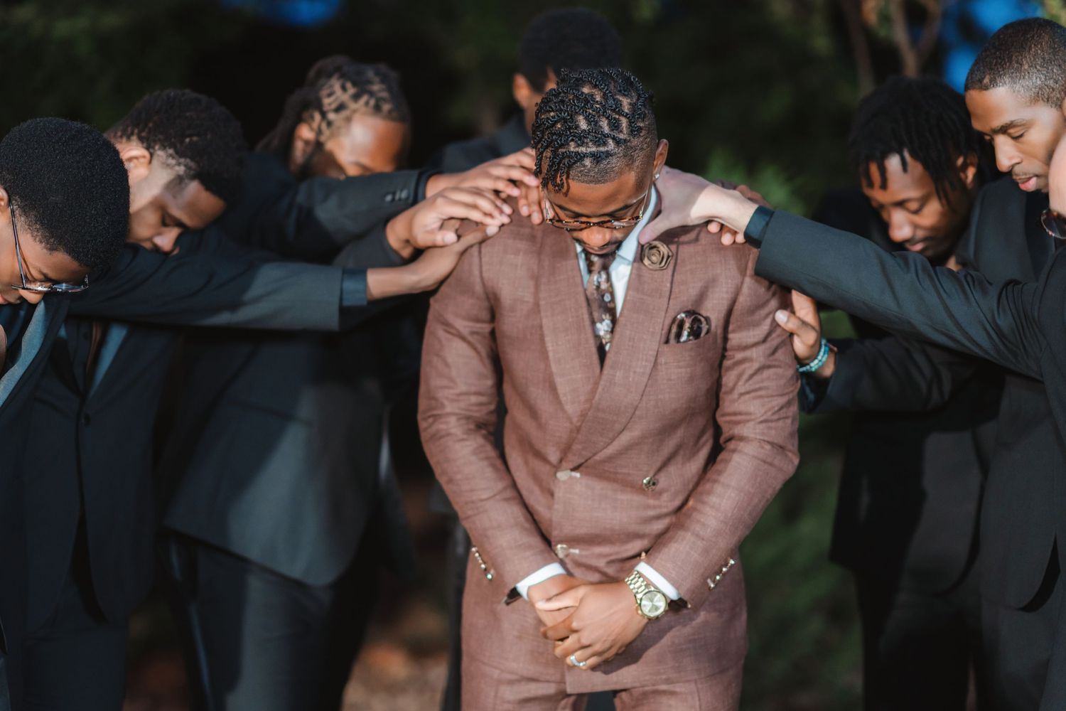 Wedding party poses together outdoors wearing formal attire in brown and black.