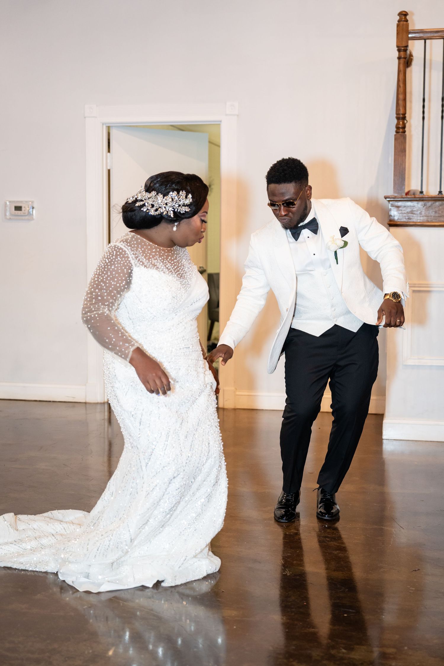 A joyful couple dancing together at their wedding reception, with the bride in a lace gown and groom in white tuxedo.