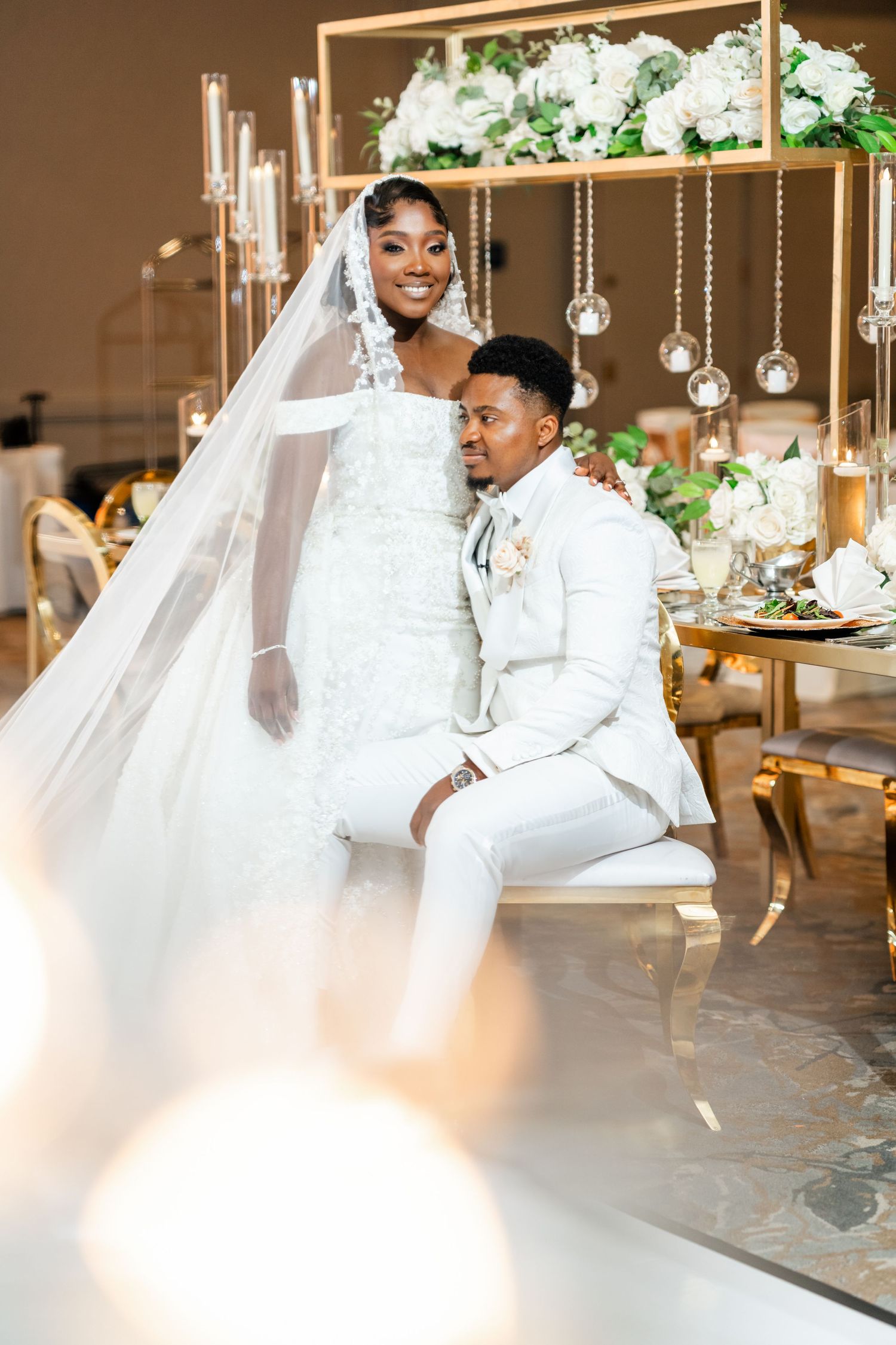 Elegant wedding scene with a couple seated at a luxurious table decorated with hanging crystal ornaments and greenery.