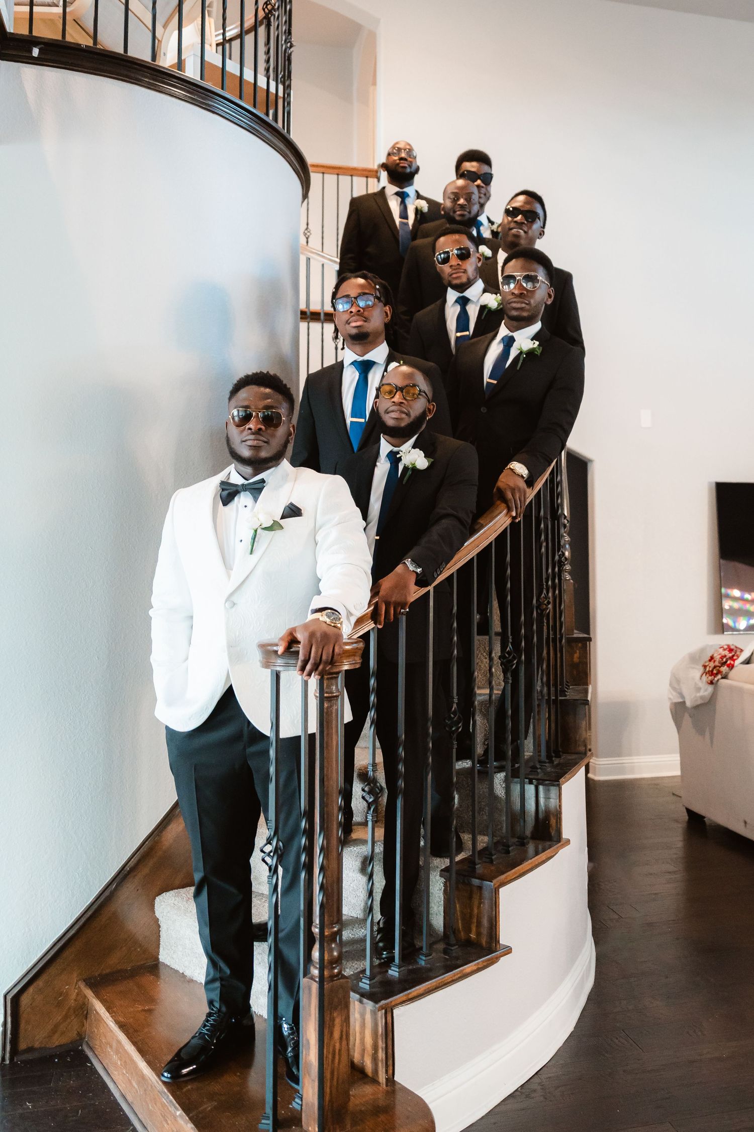 Wedding party in black and white tuxedos posed on elegant staircase.