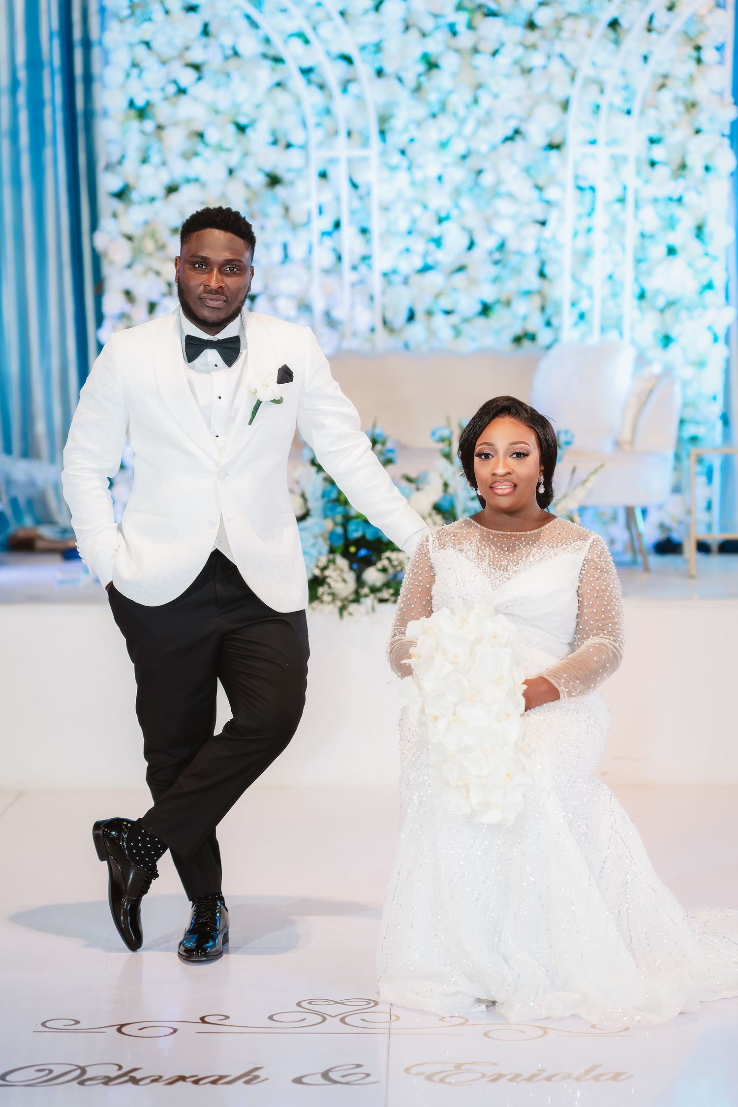 Elegant wedding couple poses in front of a blue and white floral backdrop during their celebration.