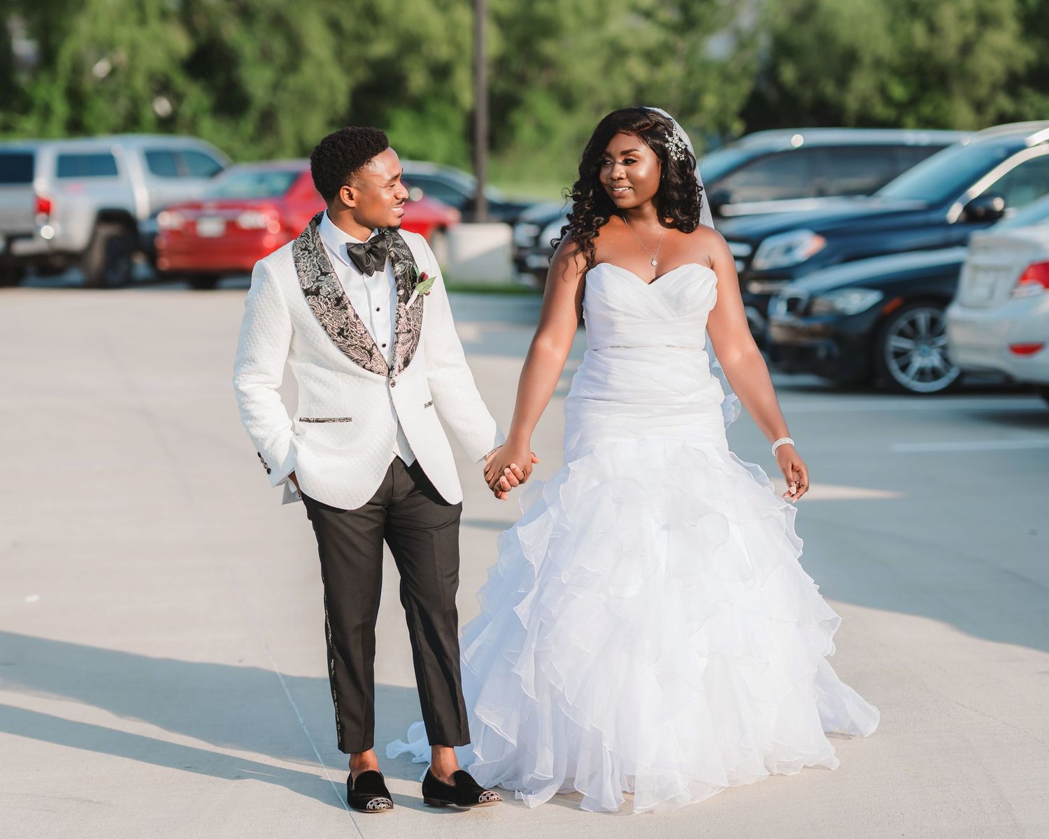 A couple in formal wedding attire walks together through a parking lot on their special day.