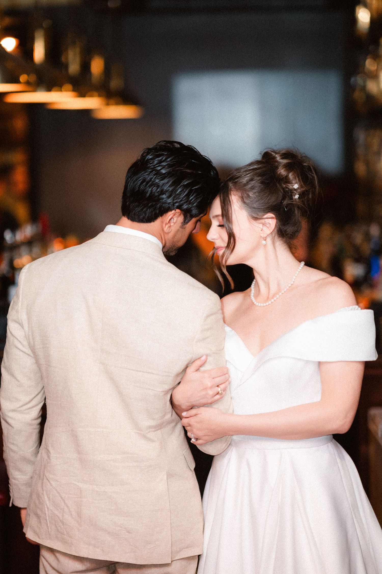 A couple shares an intimate embrace in formal attire against a dark indoor background.