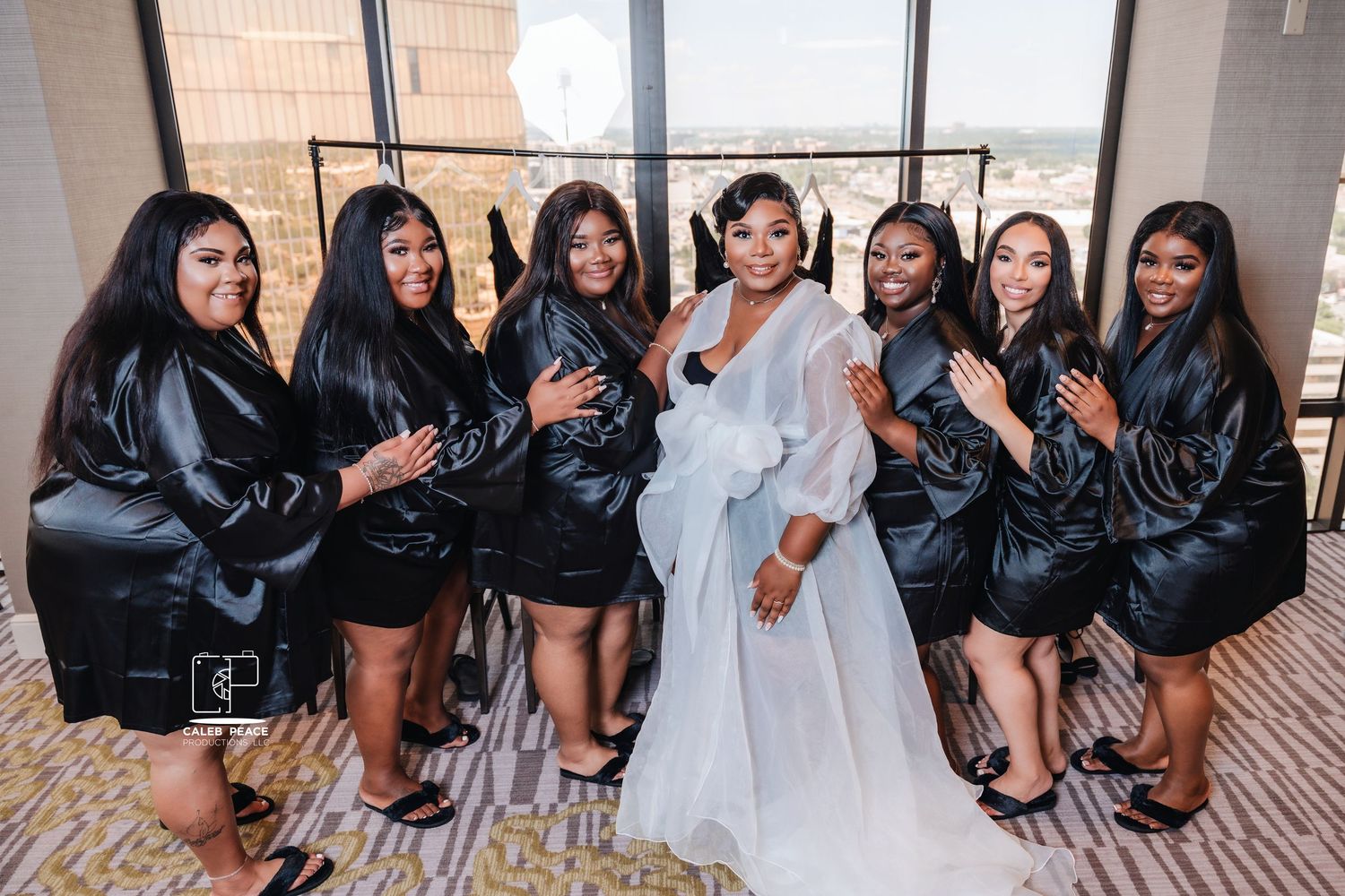 Bridal party in matching black robes posing with the bride in white robe.