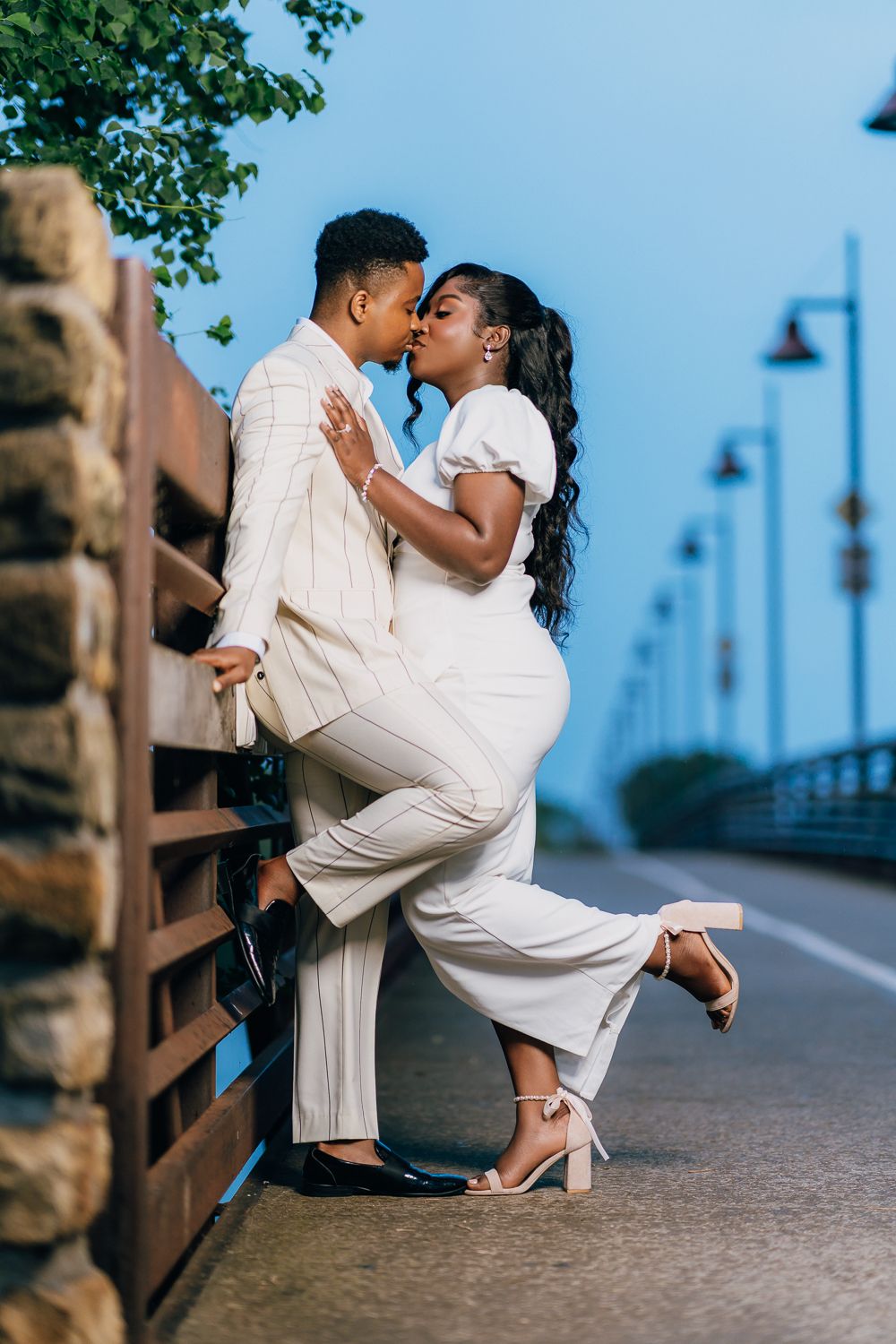 A couple shares an intimate dance pose on an outdoor walkway with blue sky in the background.
