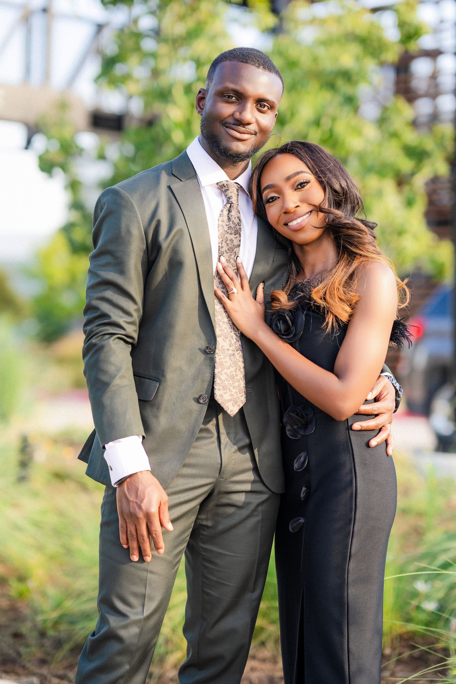 Couple in coordinated formal wear posing together in outdoor garden setting.
