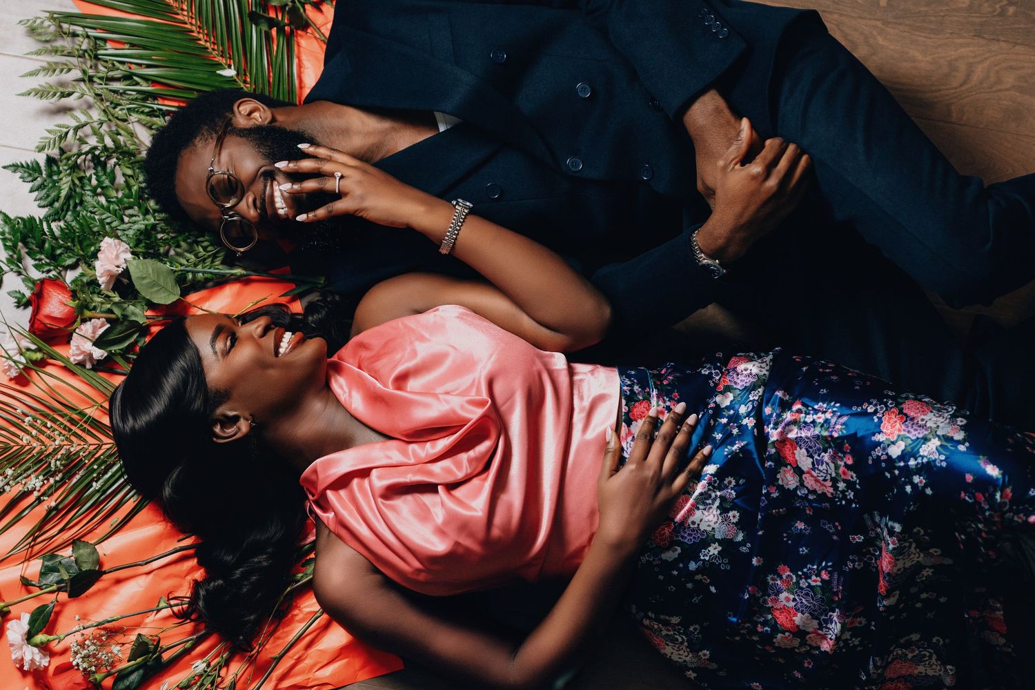Romantic couple lying on floor with palm leaves and roses in elegant evening attire.