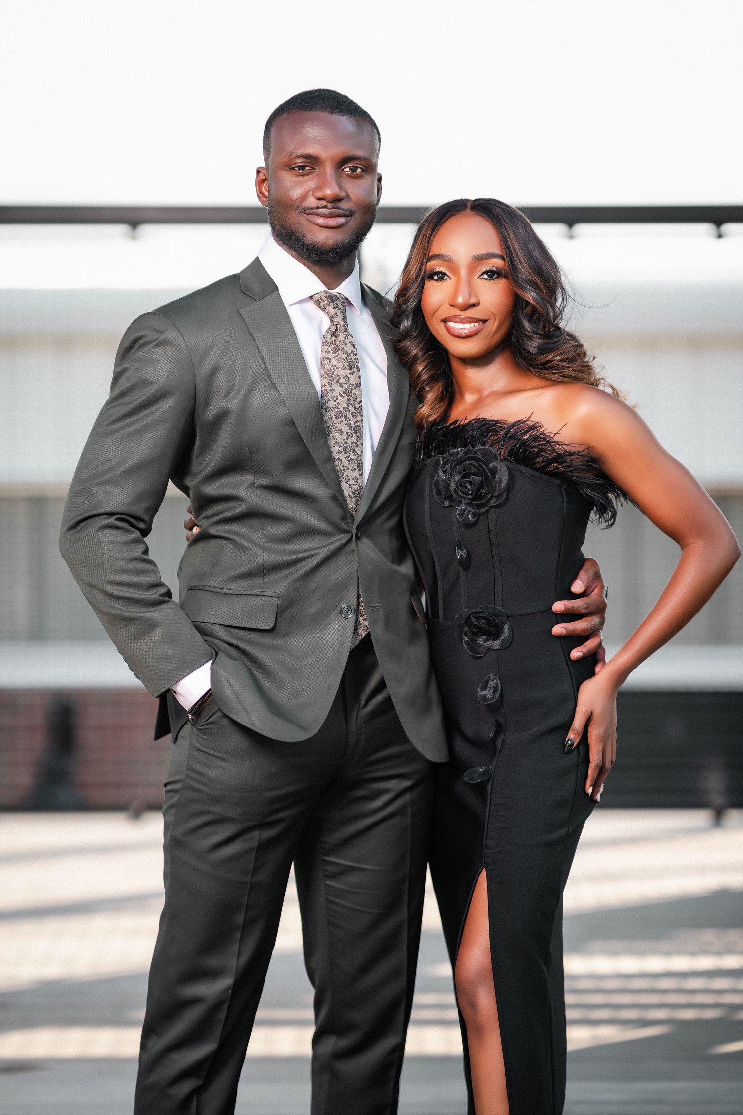 Stylish couple in formal wear posing together against modern architectural backdrop.