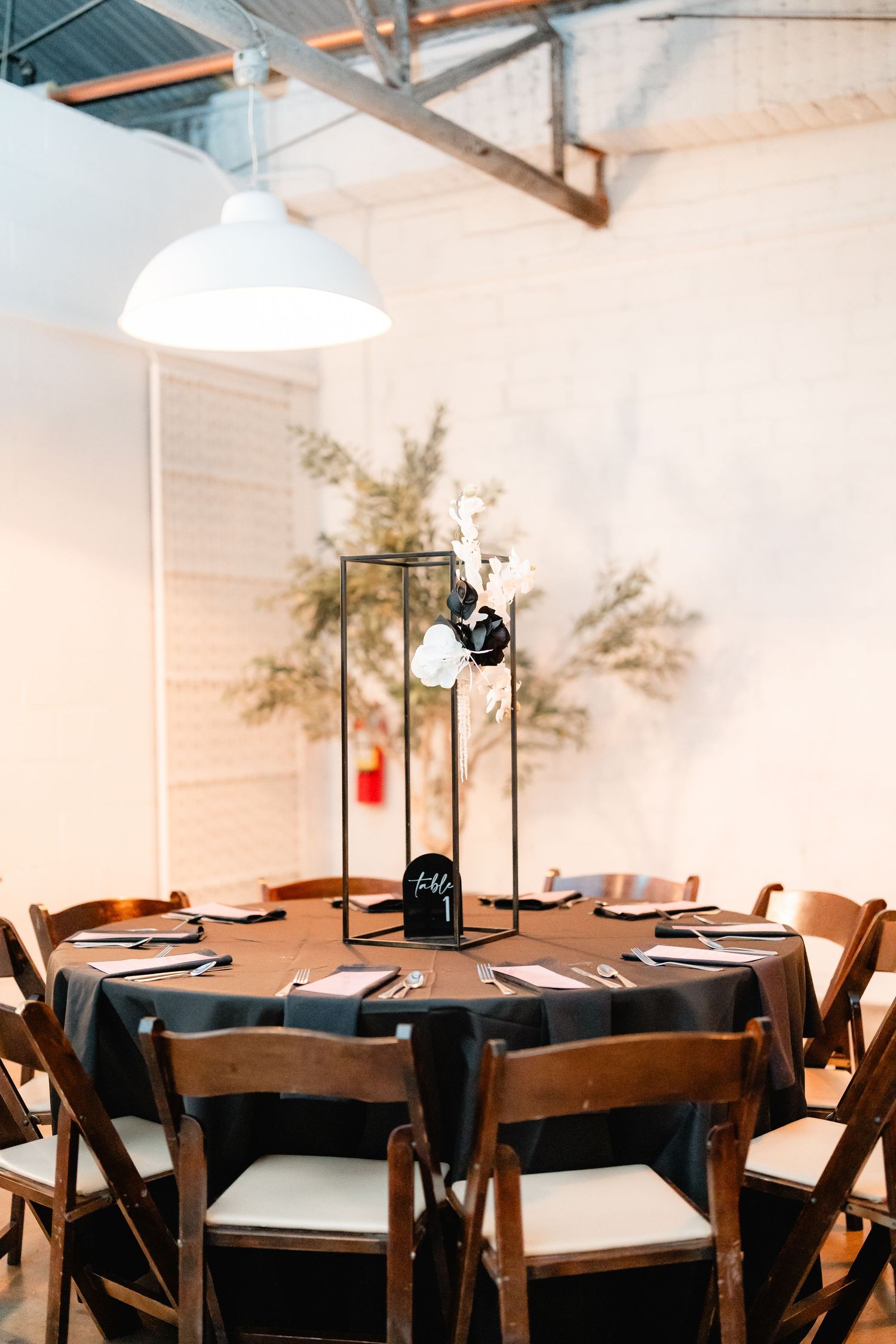 Wedding reception tables set with dark linens and black lantern centerpieces in an industrial space.