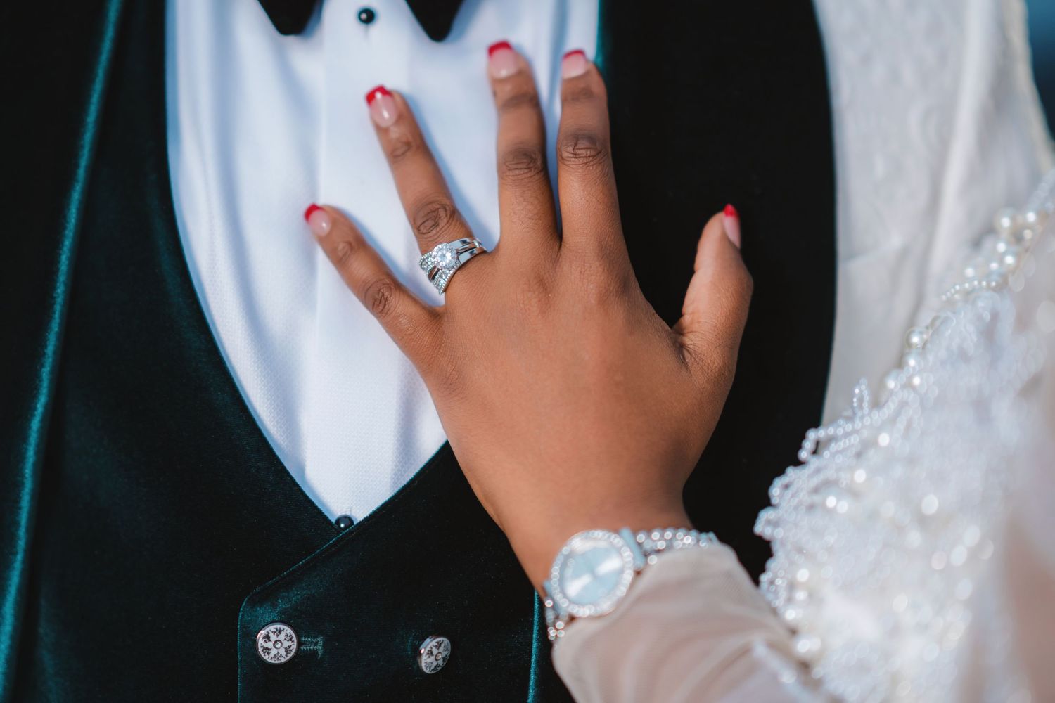 Close-up view of hands adjusting a white wedding dress with delicate beaded details and lace embellishments.