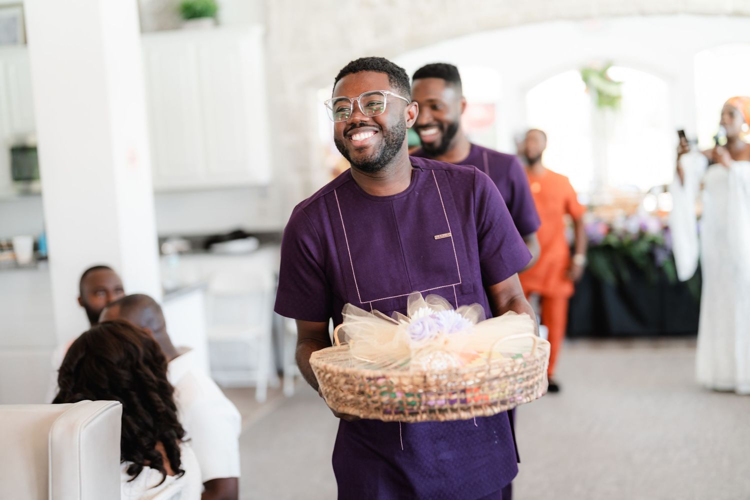 Wedding guests in purple and orange attire enjoying festivities in a bright indoor venue.