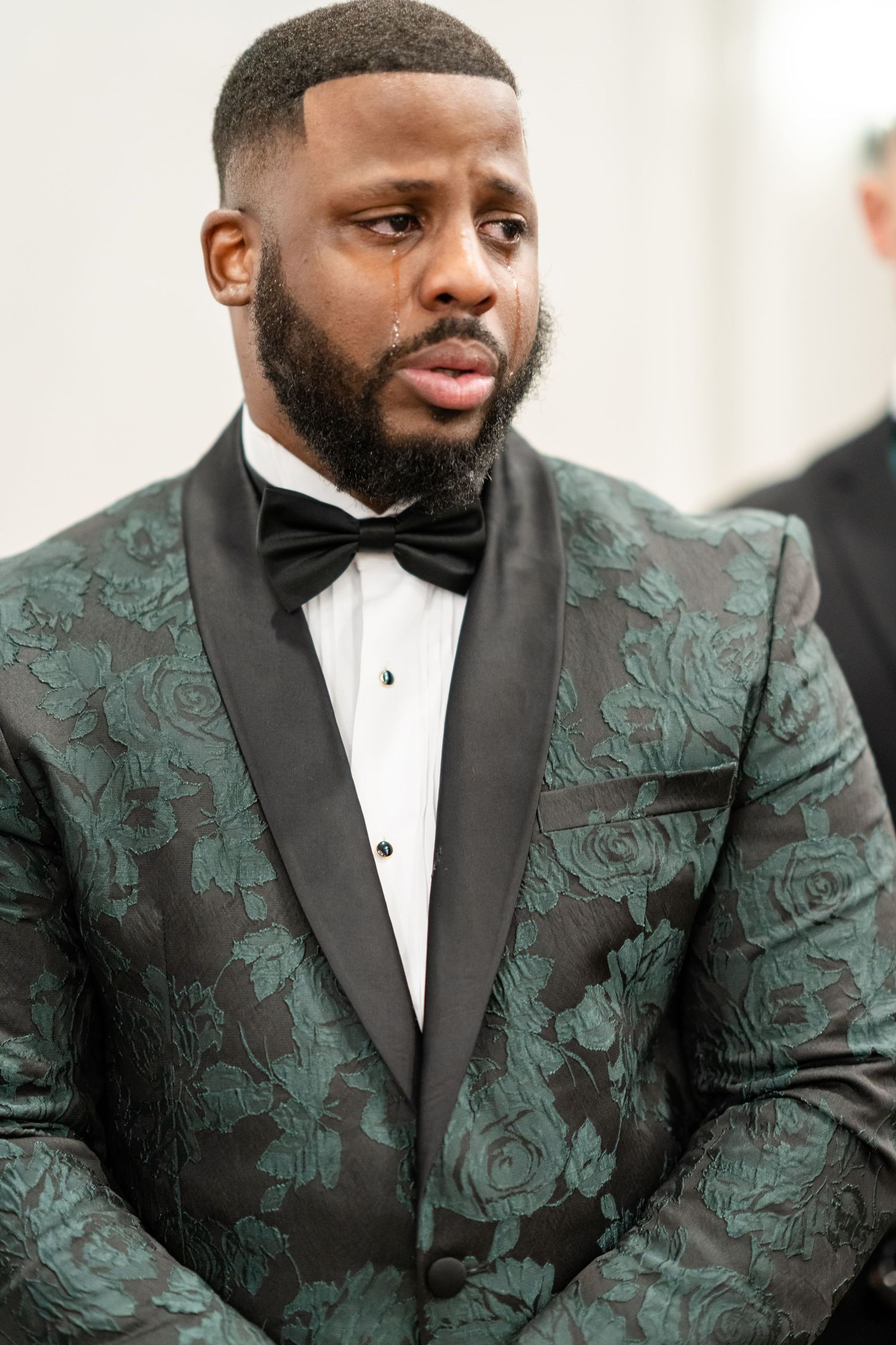 Close-up of a formal jacket with green floral brocade pattern and black lapels.