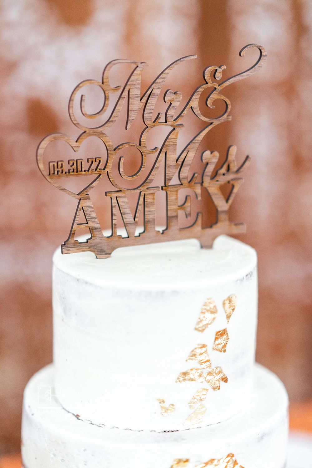 Elegant white wedding cake decorated with metallic Mr & Mrs topper and delicate details.
