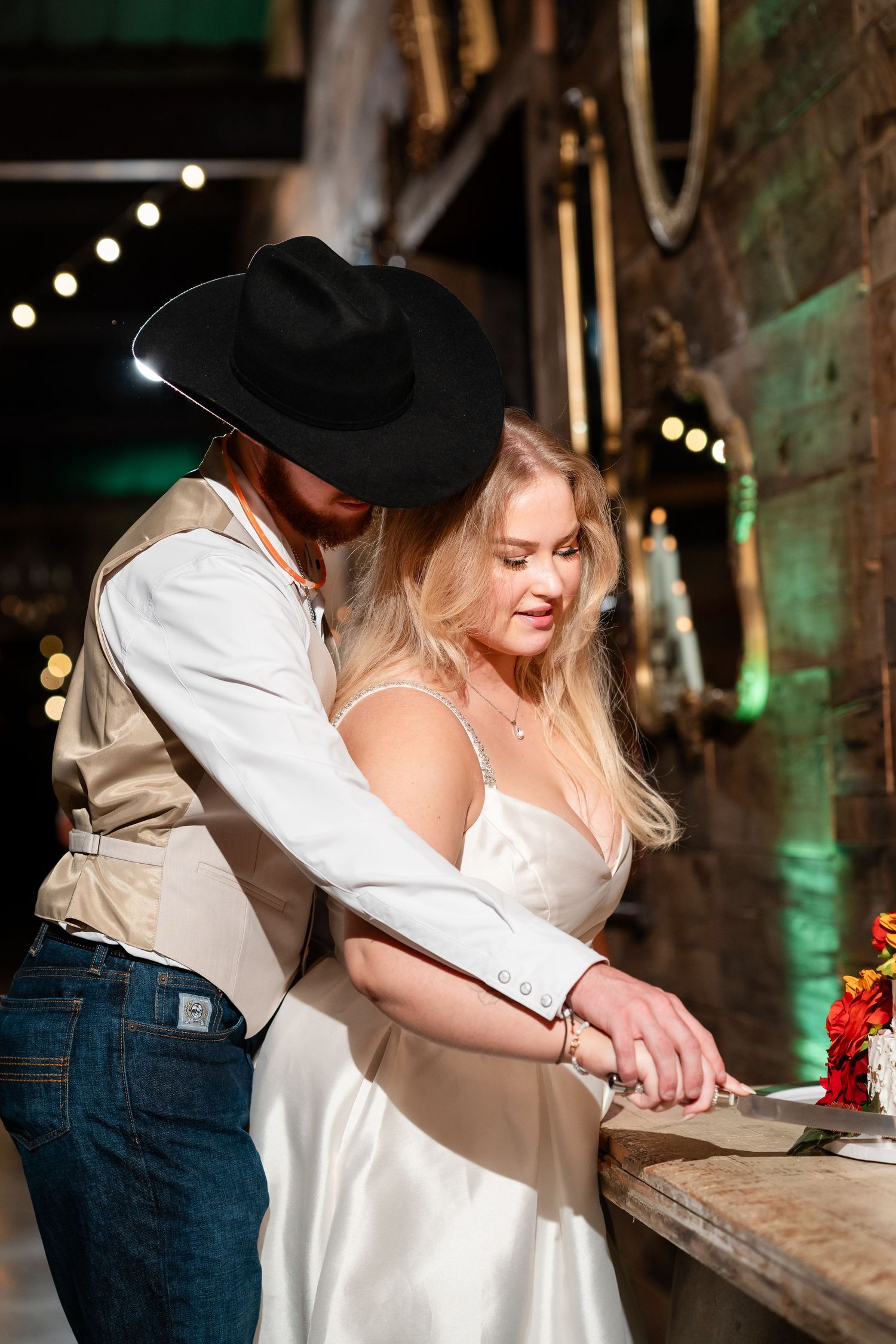 Couple shares intimate moment at rustic wooden bar during evening reception.