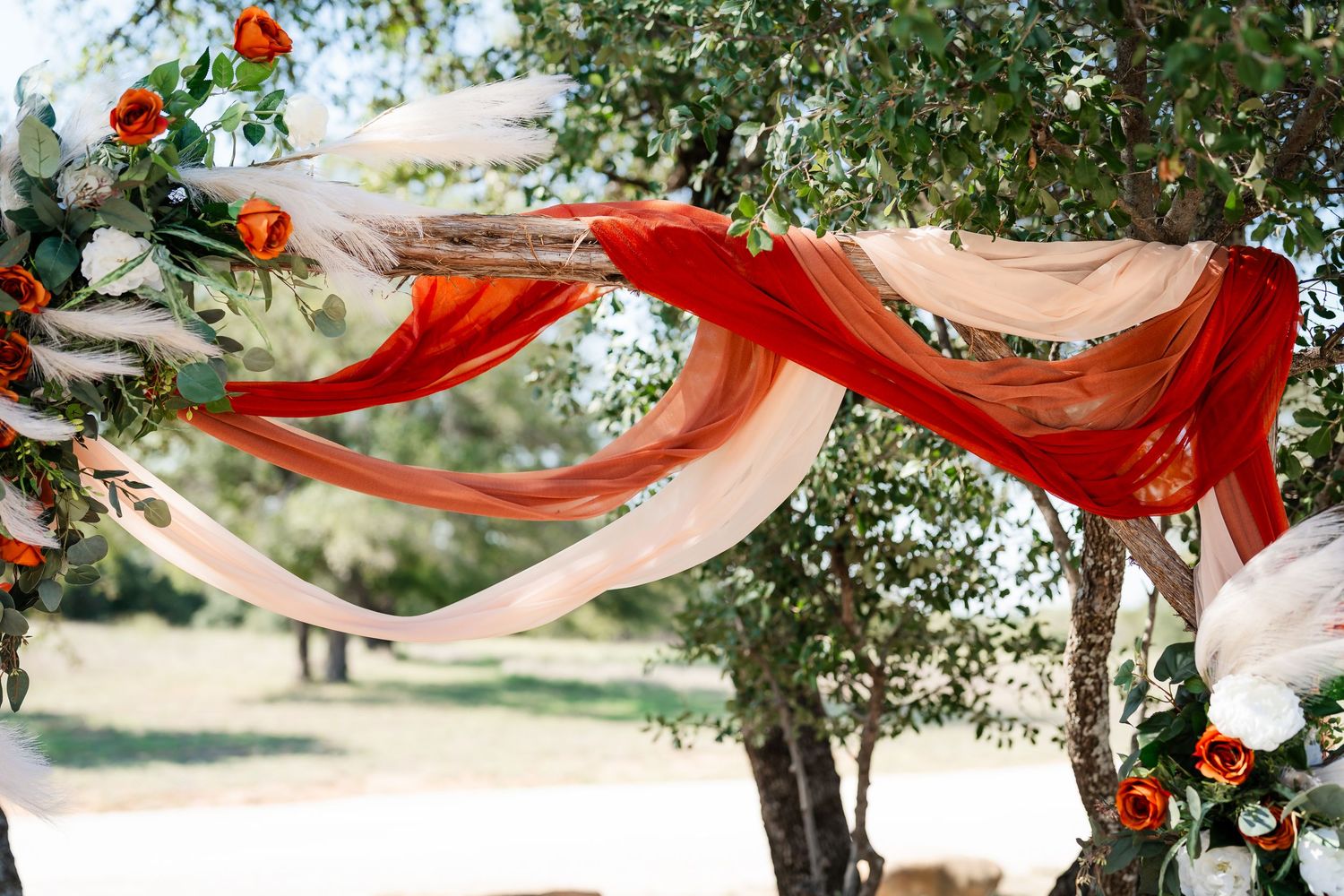 Outdoor wedding ceremony setup with red floral decorations and white fabric draping between trees.