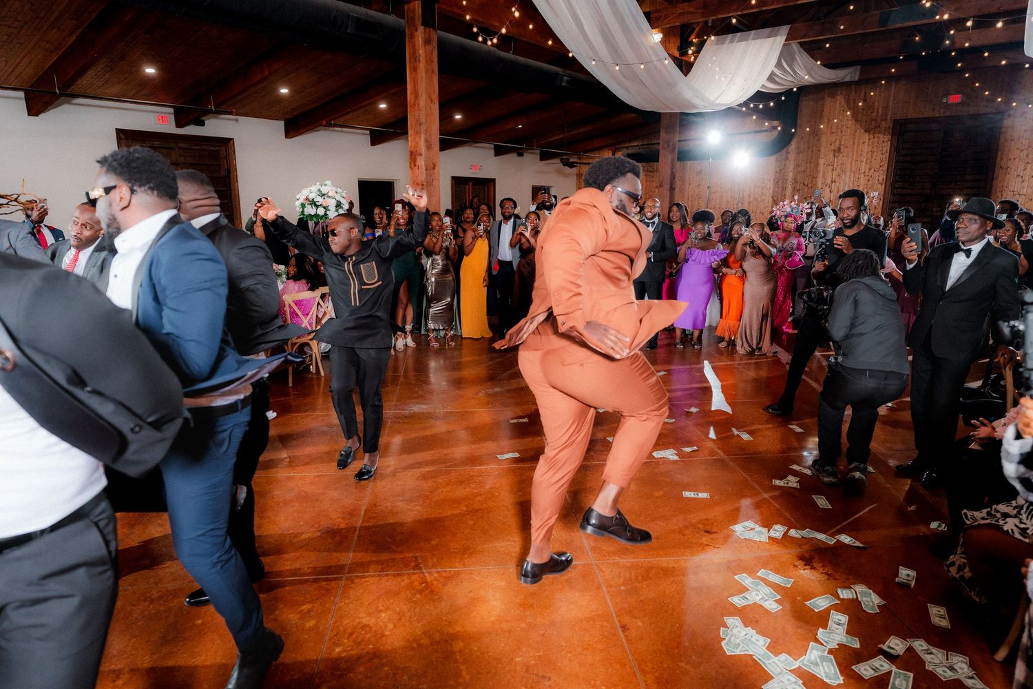 Wedding guests dance and celebrate on a wooden dance floor at a lively indoor reception party.