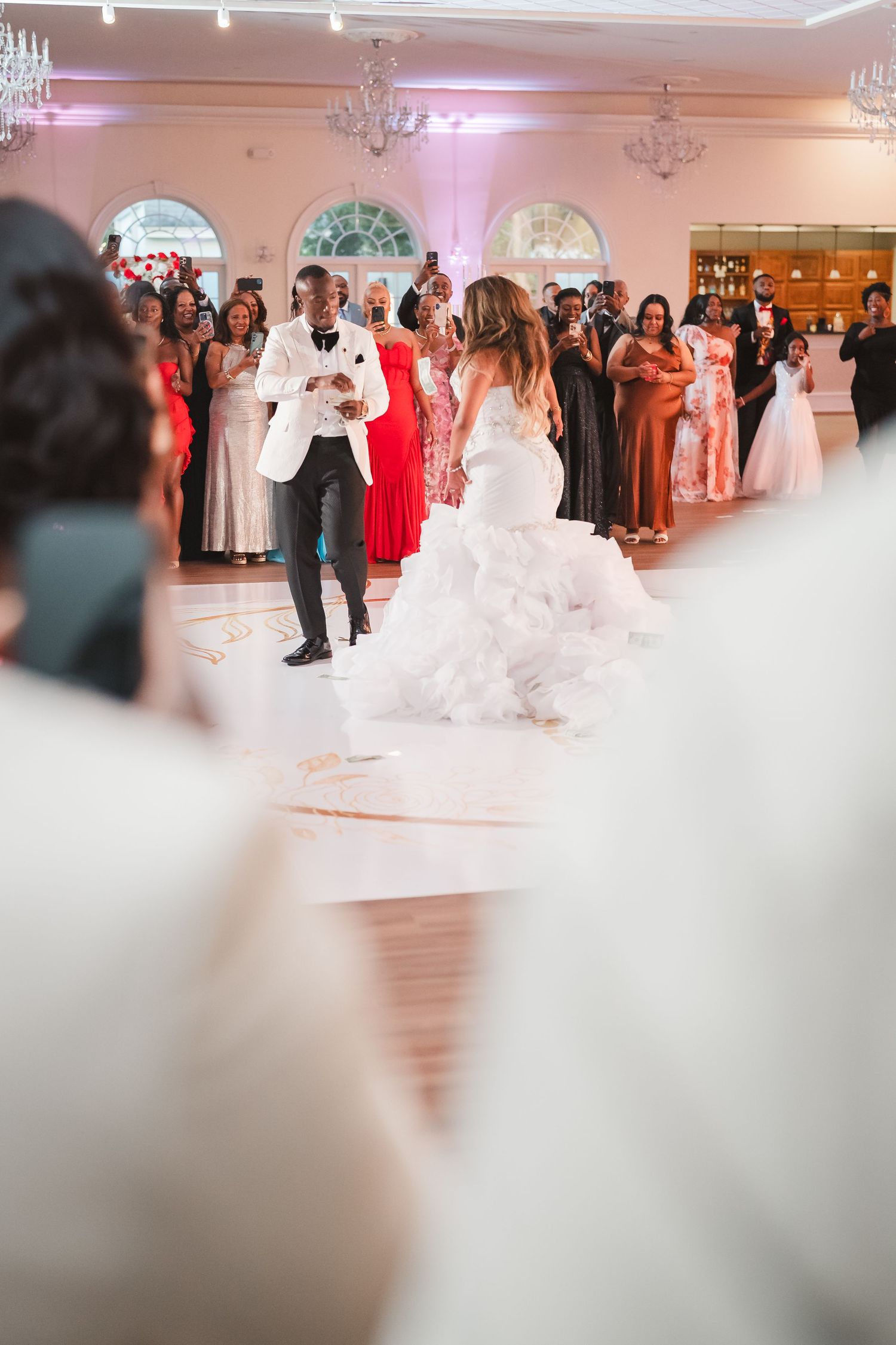 Wedding reception venue with pink lighting and chandeliers as guests gather on the dance floor.