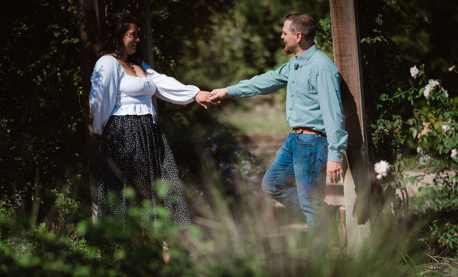 Two people share a tender moment while walking through a scenic garden pathway.