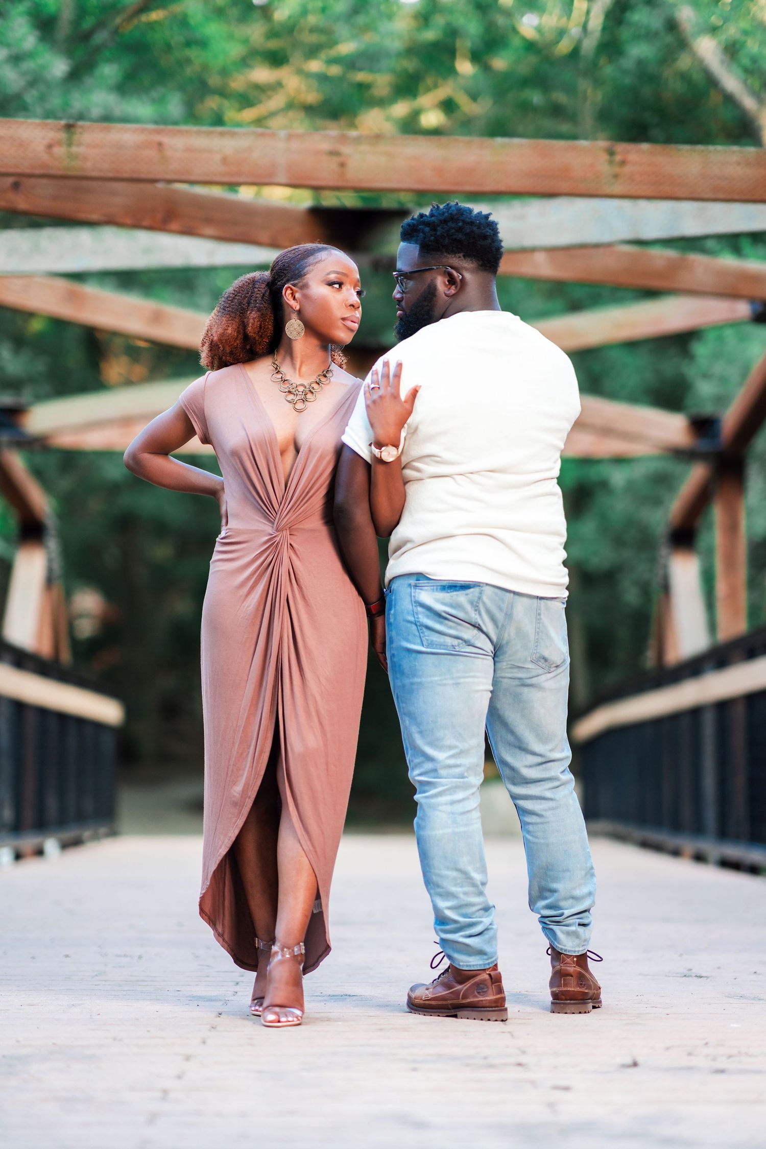 A couple stands together on a wooden bridge during a romantic outdoor photoshoot.