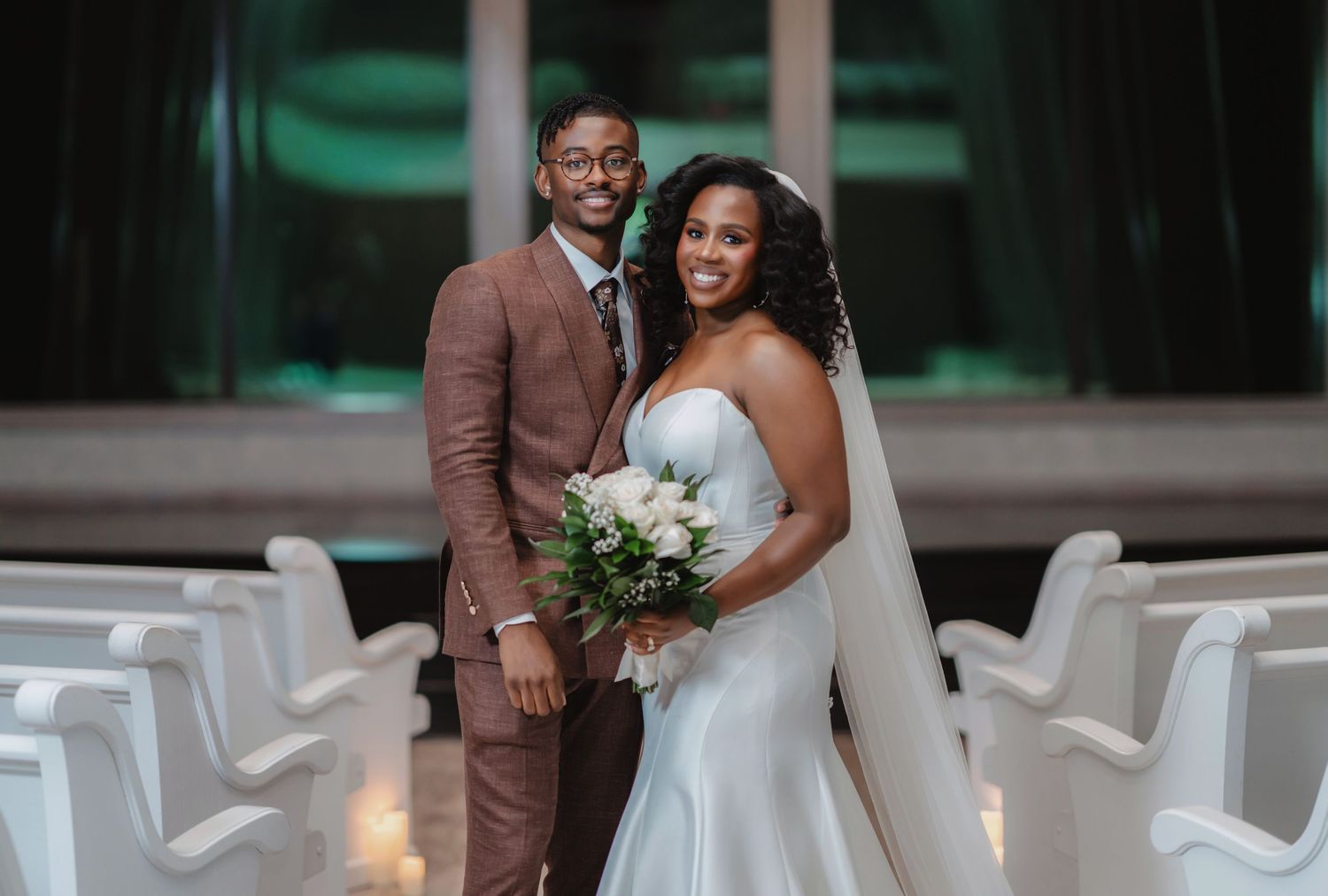 Wedding couple shares intimate moment in elegant venue with white chairs and soft lighting.