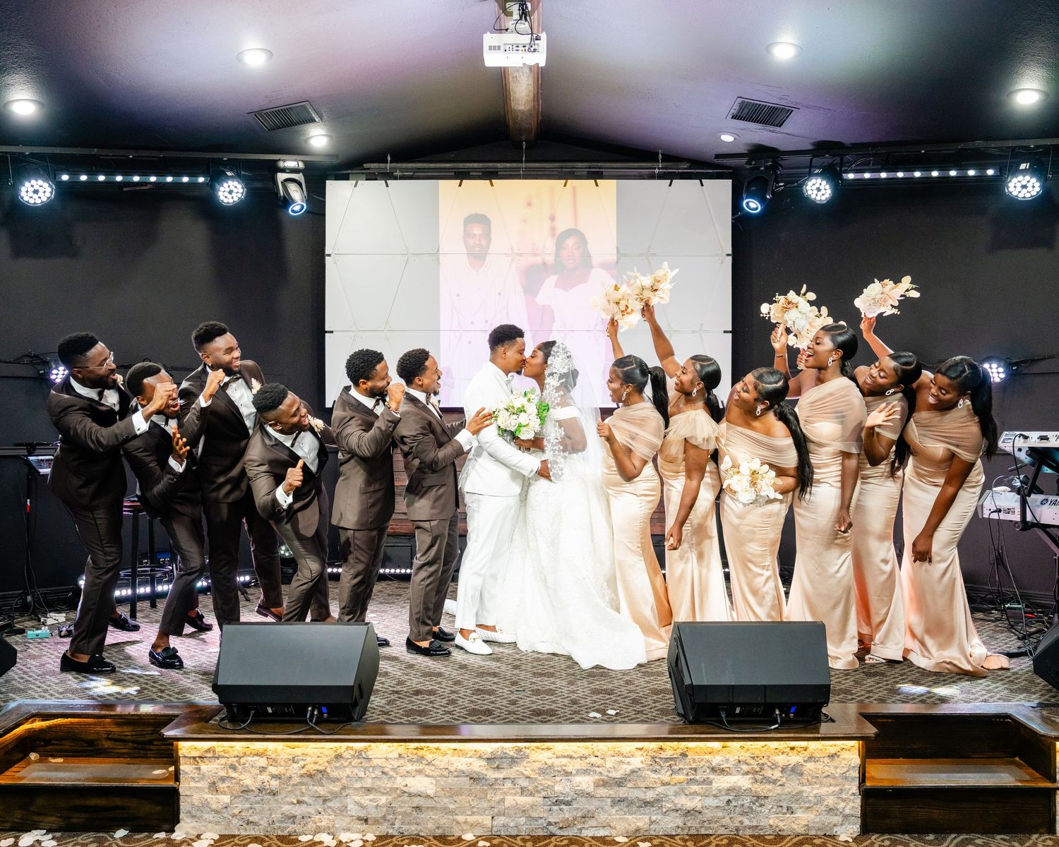 Wedding party celebration on stage with bridesmaids in champagne dresses and groomsmen in dark suits.