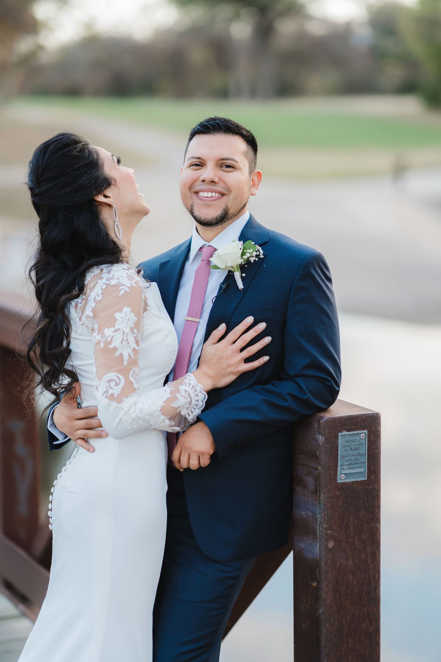 A newlywed couple shares romantic moments against a rustic wooden fence.