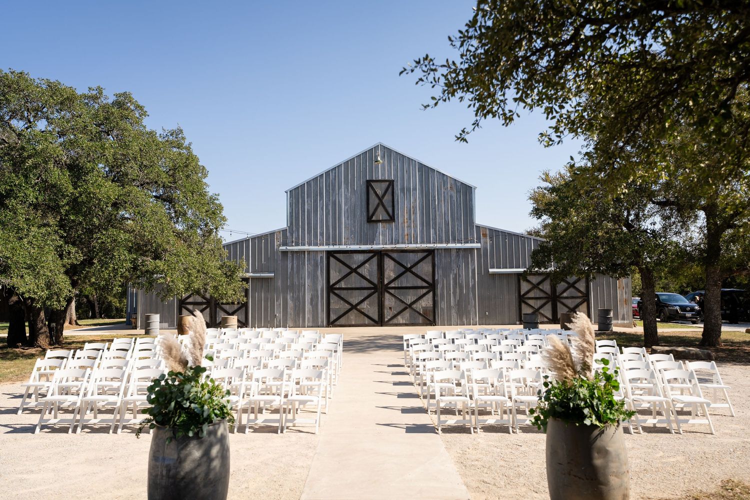 Gray barn wedding venue with white ceremony chairs set up on lawn.