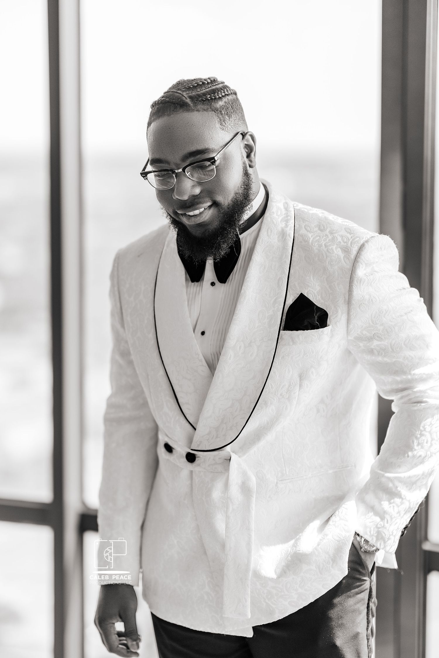 Groom in a crisp white tuxedo jacket with black lapels and bow tie smiles during wedding preparations.