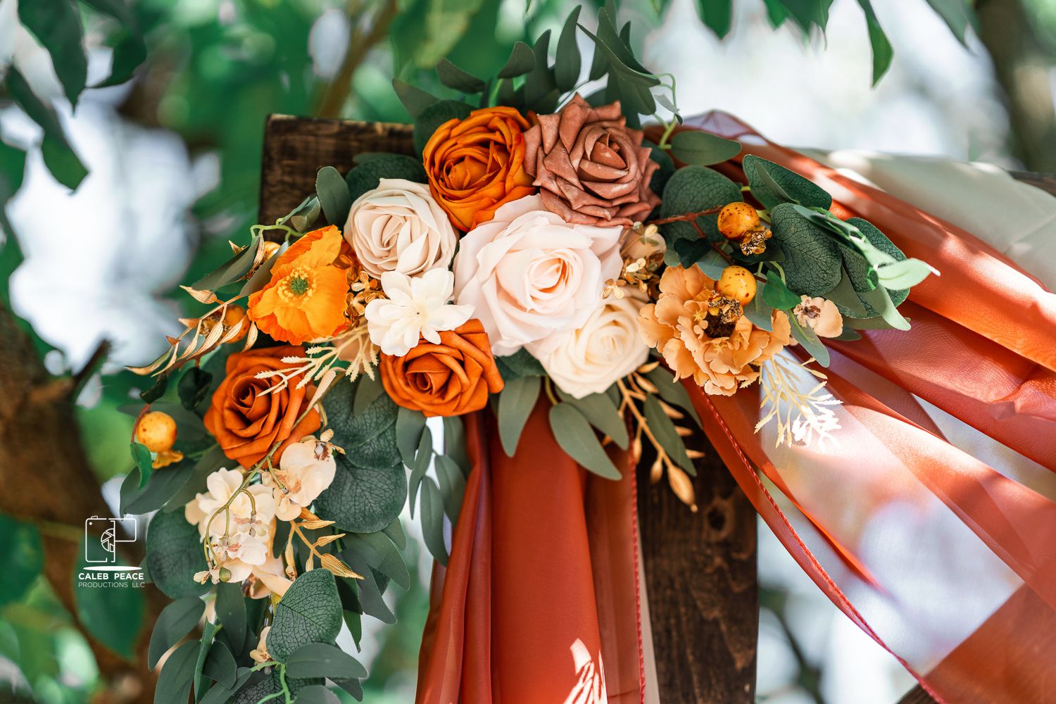 Terracotta and peach colored floral wedding arch decorations with roses and greenery against a white backdrop.