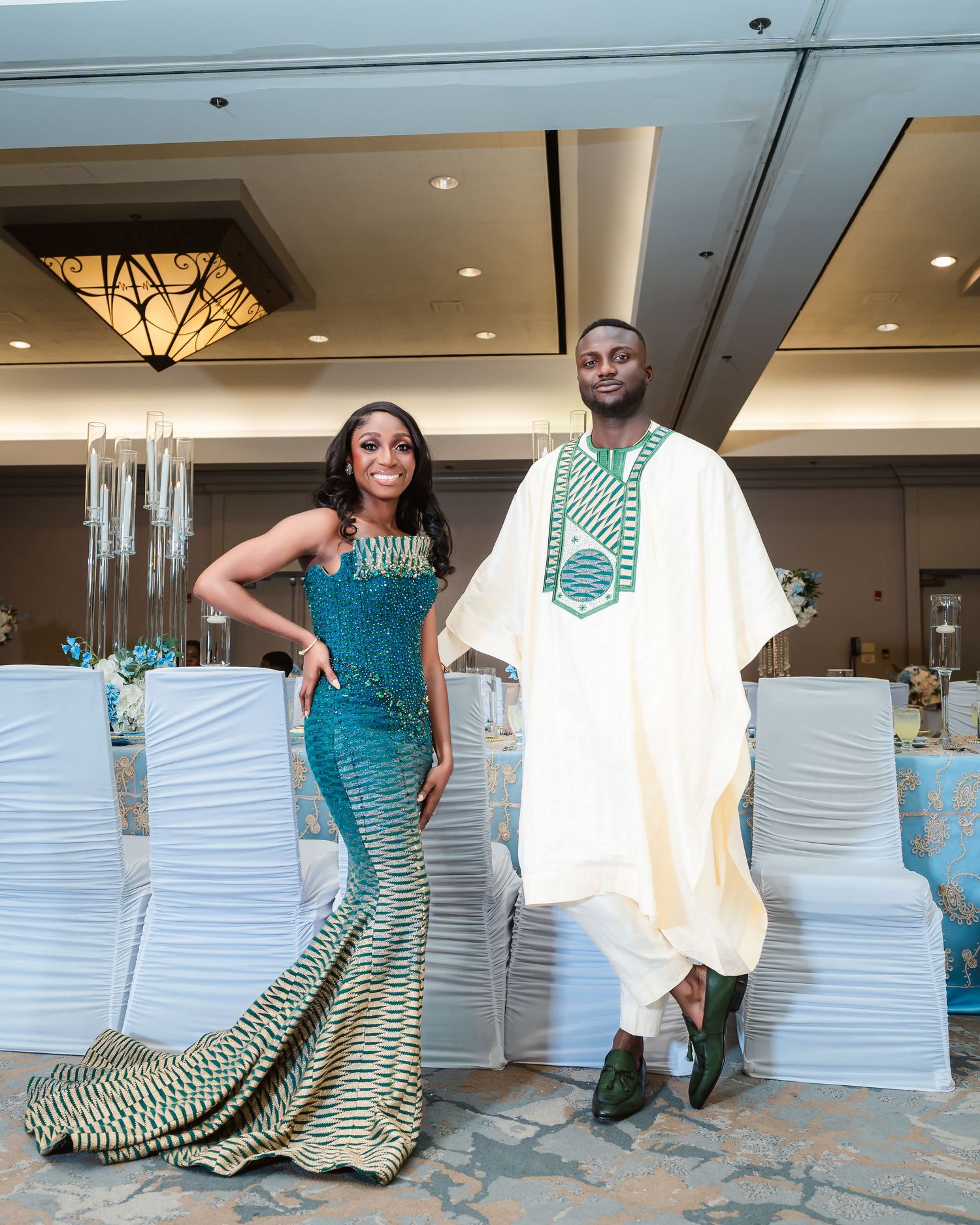 A couple poses in elegant Nigerian wedding attire featuring green and white patterns at their reception venue.