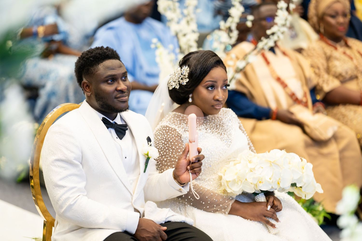 Wedding ceremony scene with couple seated in elegant white and gold attire.