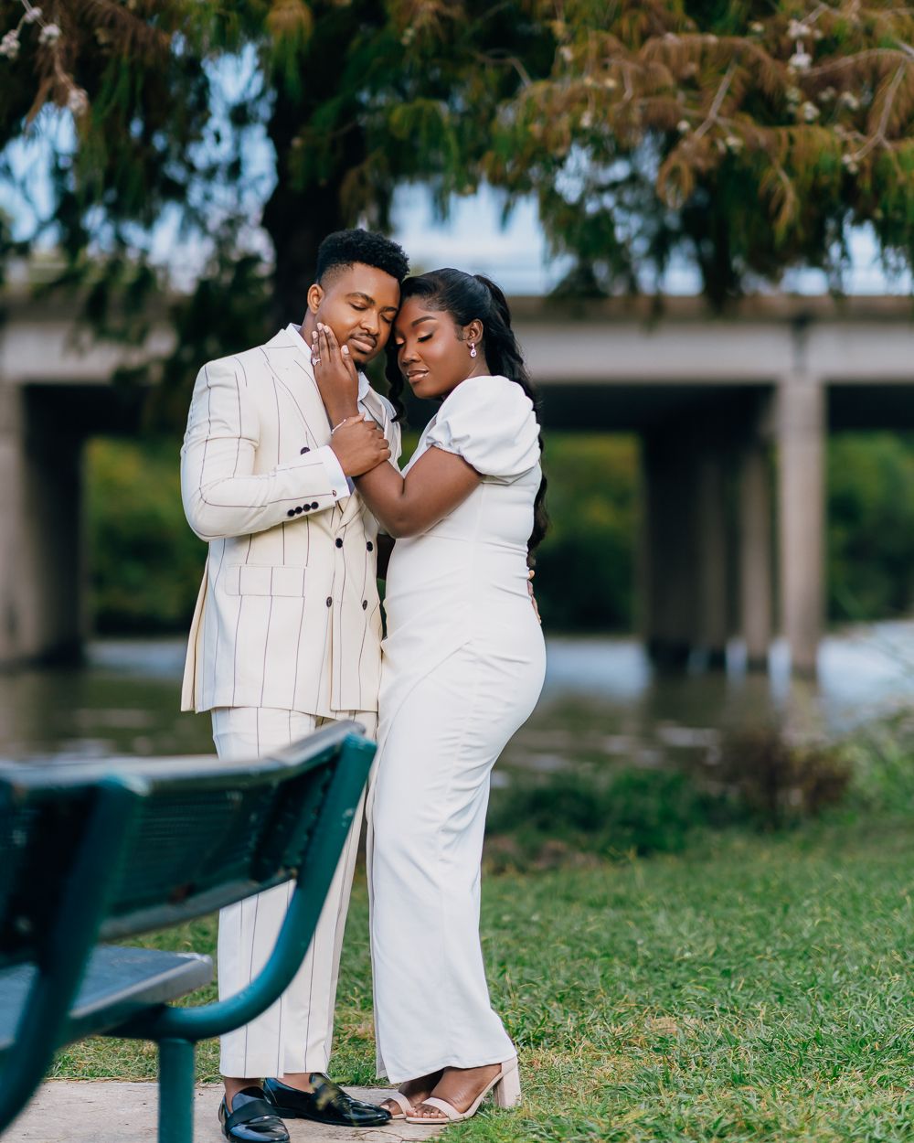 A couple shares an intimate moment outdoors while posing for engagement photos in a park setting.