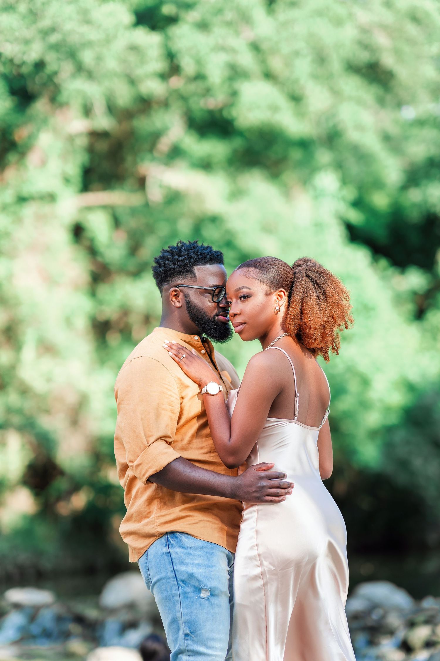 A romantic couple shares intimate moments in a natural outdoor setting with green foliage in the background.