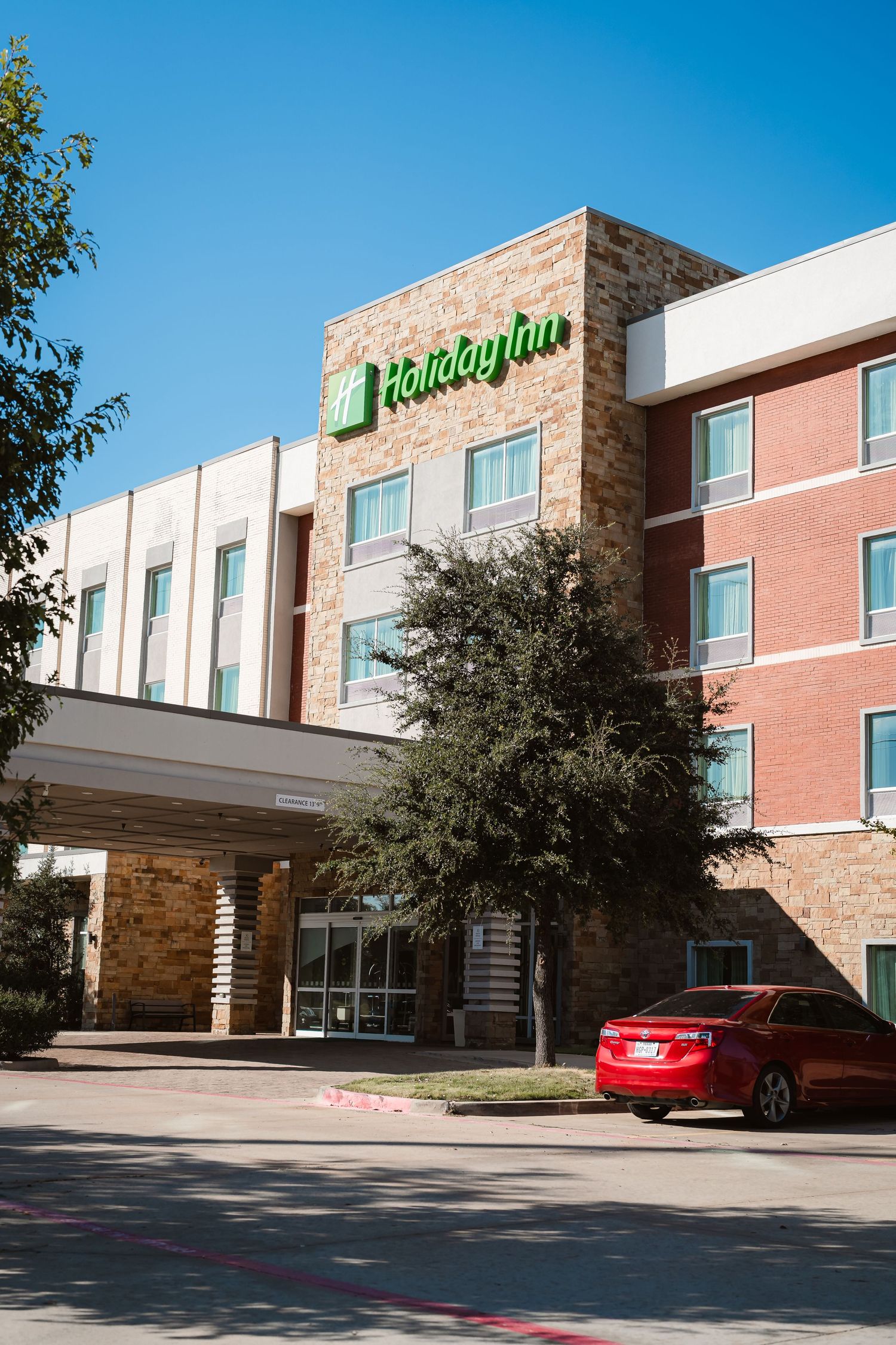 Holiday Inn hotel exterior with red brick and stone facade shown from multiple angles in bright daylight.