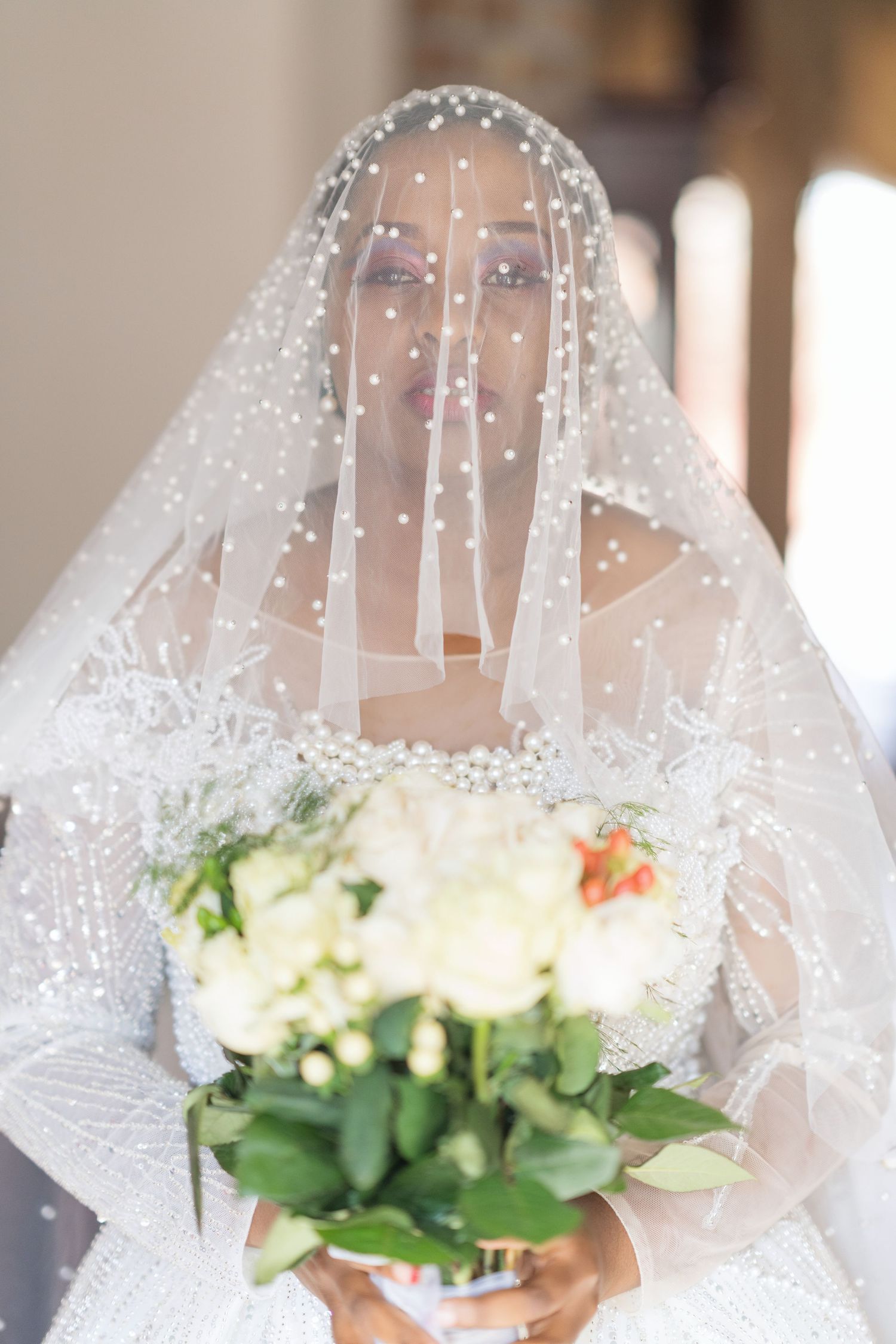 A delicate pearl-studded wedding veil frames a classic white bridal bouquet.
