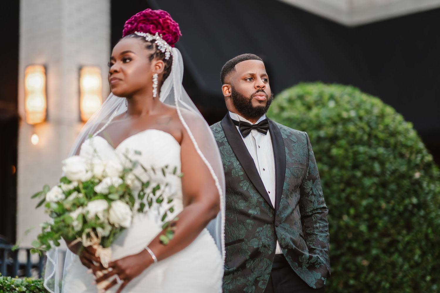 A stunning wedding portrait features a couple in elegant attire against a backdrop of greenery and warm lighting.