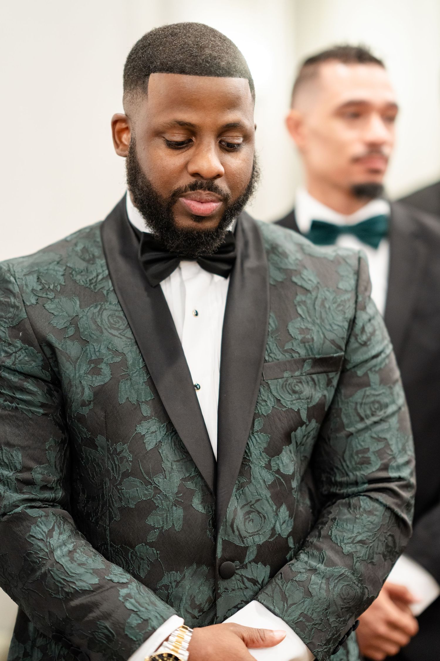 A groom wearing an elegant green floral jacquard tuxedo jacket with black lapels.