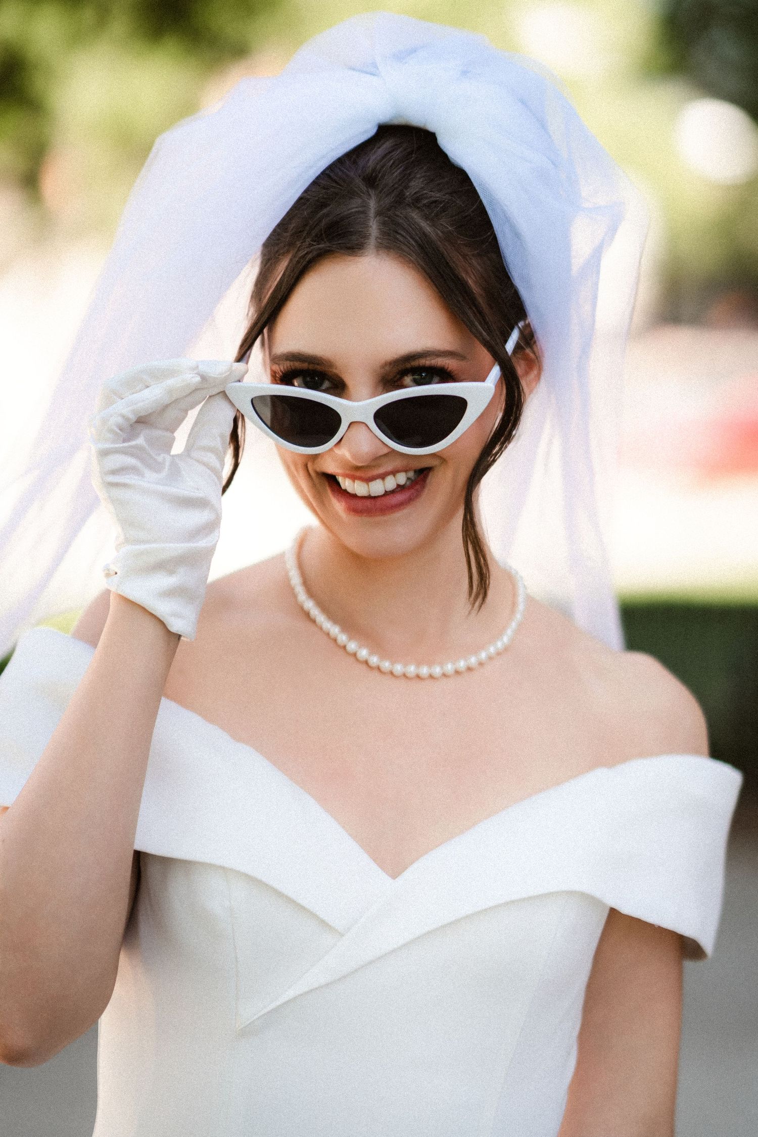 Bride wearing vintage-style sunglasses and pearl necklace with white wedding dress.