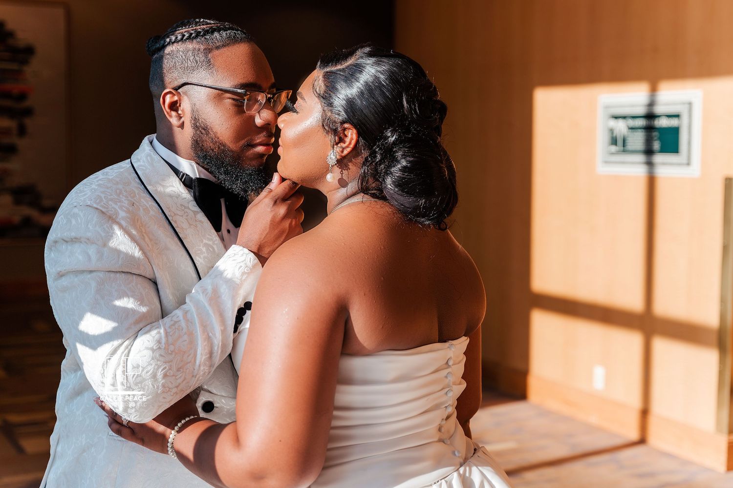 A romantic wedding couple shares a tender kiss during their special day in a warmly lit indoor setting.