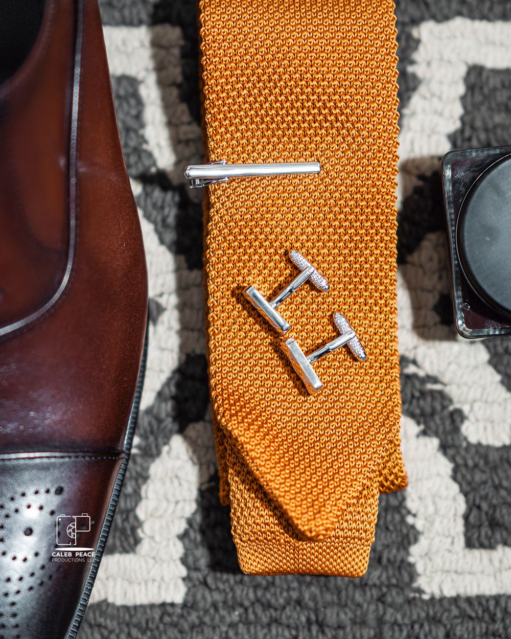 Wedding accessories including cufflinks and orange tie on patterned fabric.