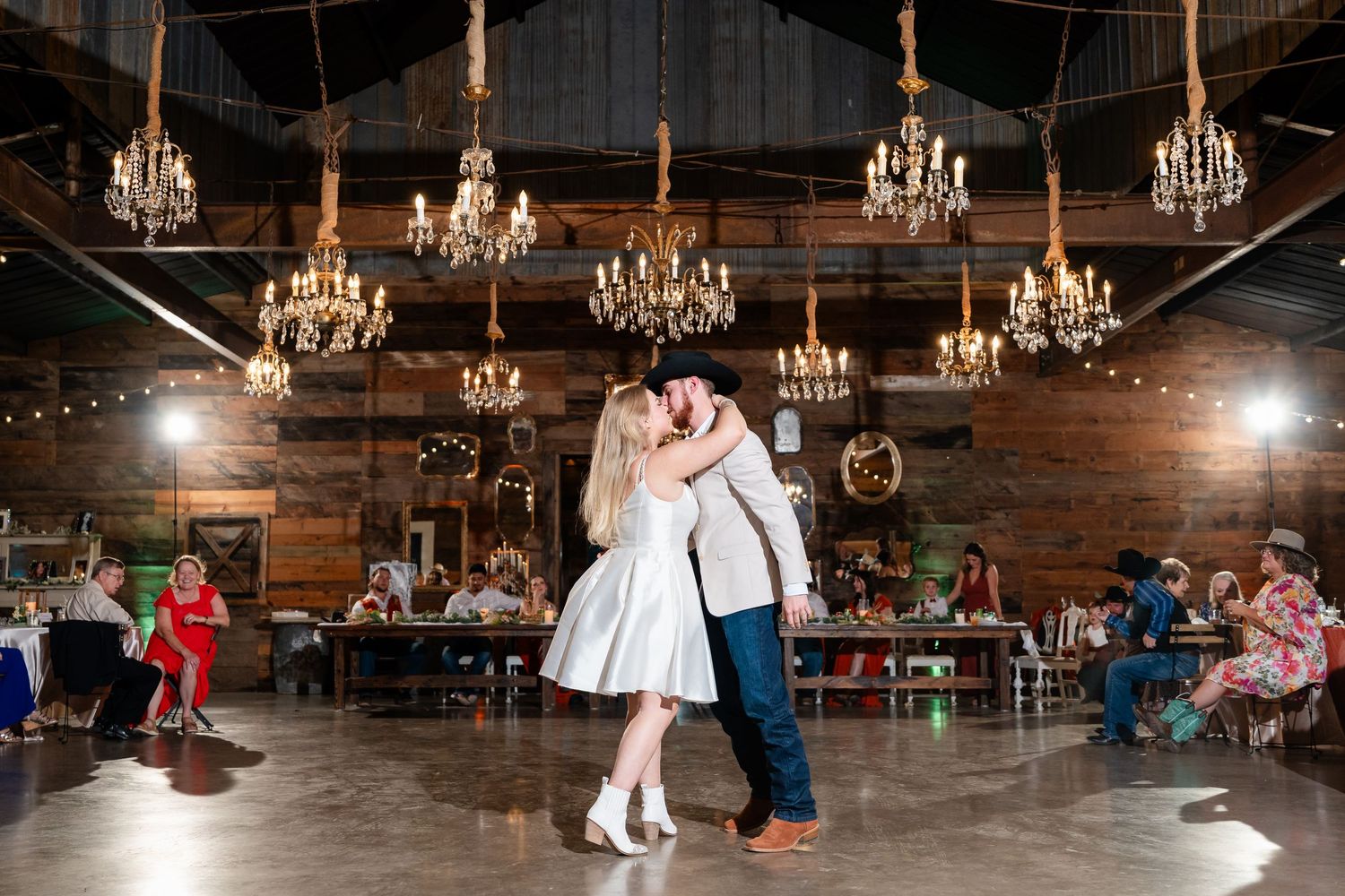 Wide view of a rustic barn wedding venue with elegant chandeliers and dancing guests.