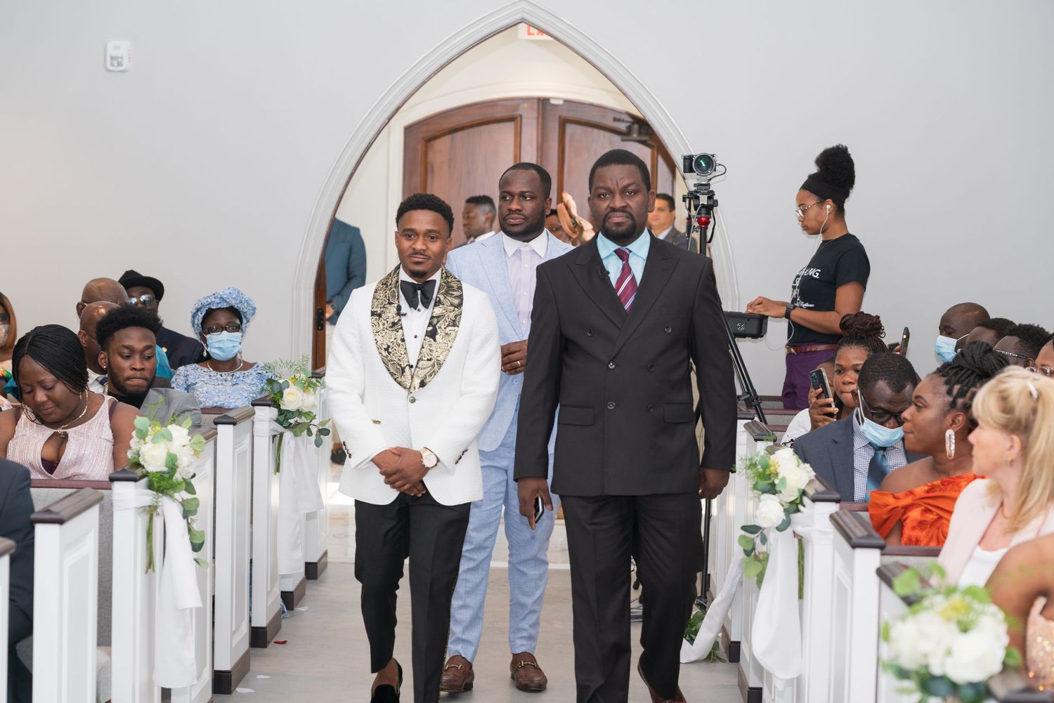 Wedding ceremony in a modern church venue with white pews and floral decorations.
