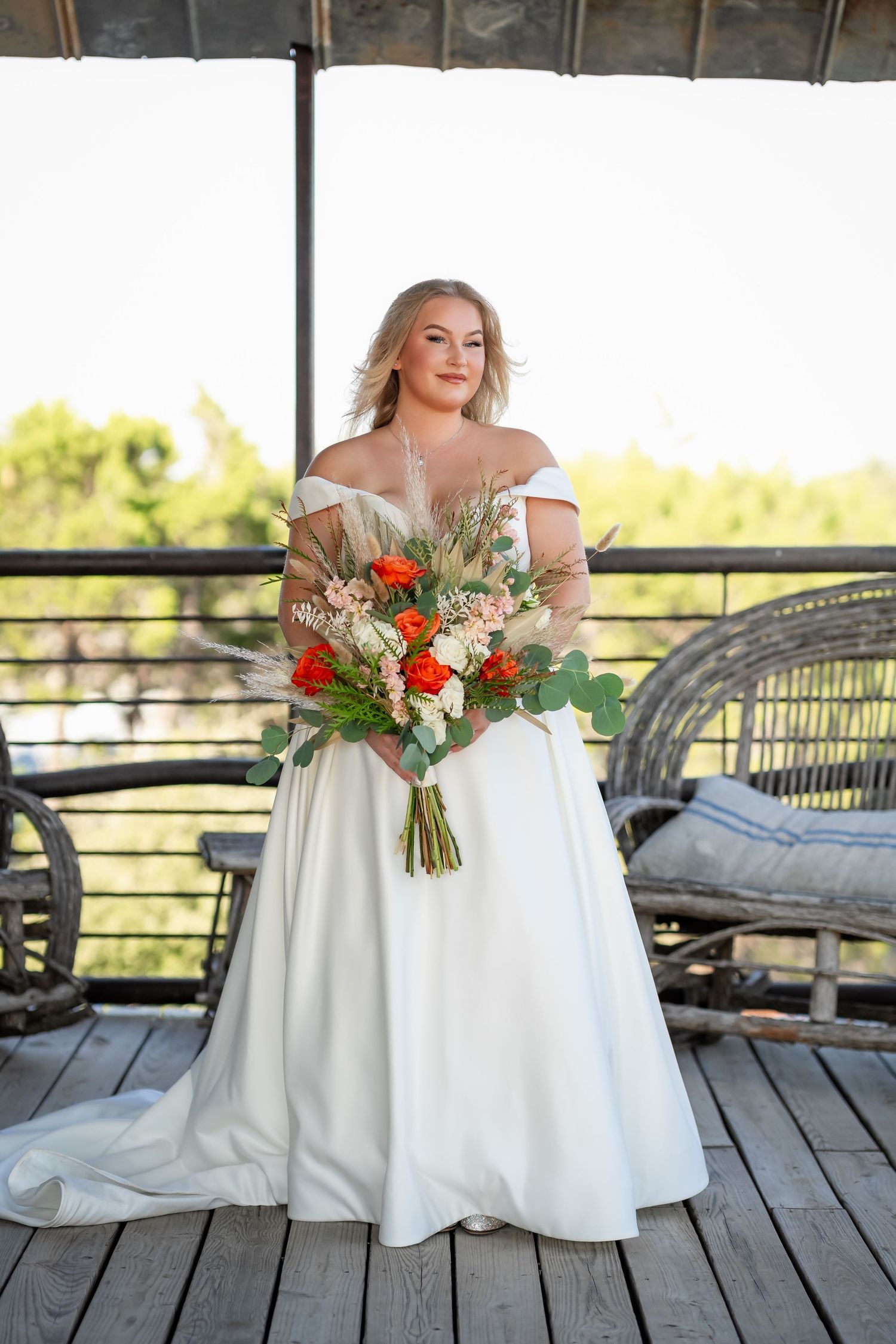 A white wedding dress and floral bouquet with orange and white flowers displayed on an outdoor deck.