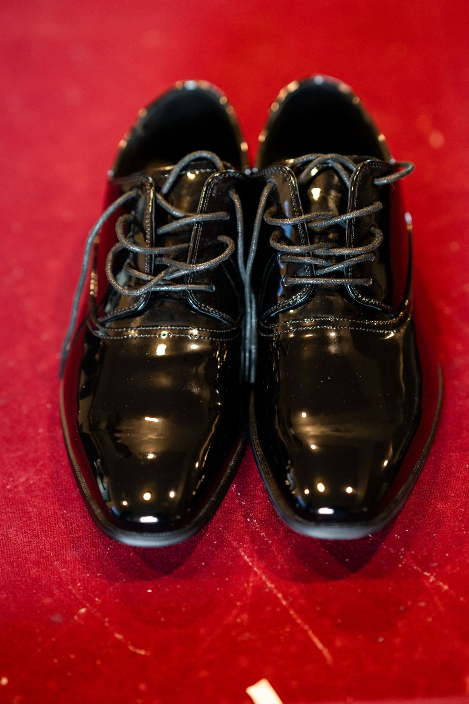 Shiny black patent leather dress shoes displayed on a red background.