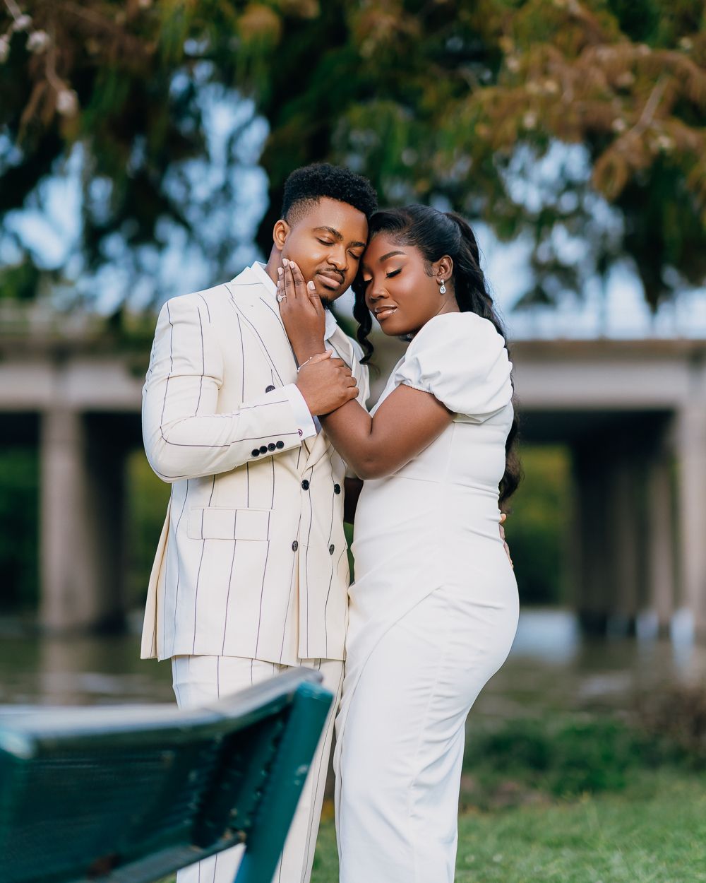 A romantic outdoor portrait of a couple in coordinating white outfits embracing tenderly against a natural background.